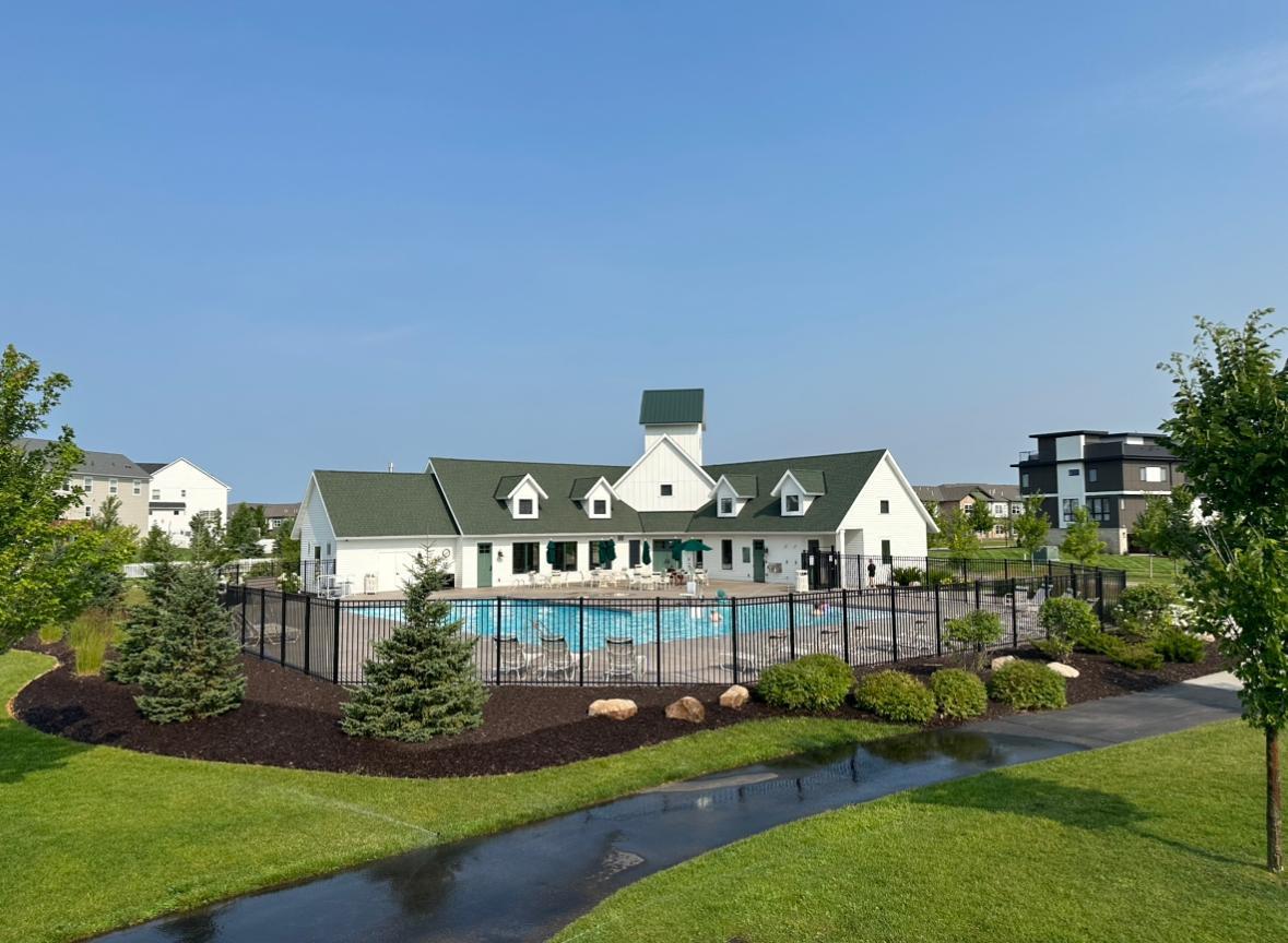 Community clubhouse and outdoor swimming pool behind a black fence, surrounded by landscaped lawn.