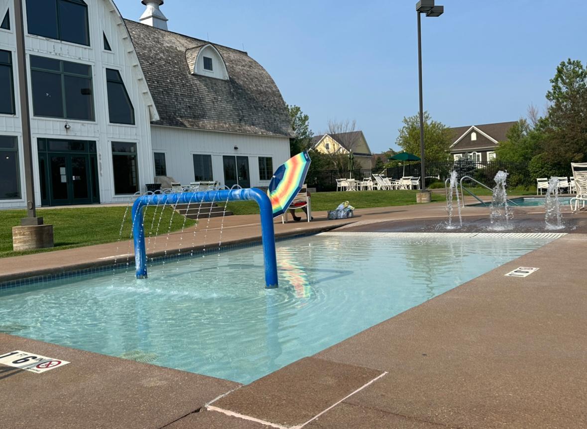 Outdoor community pool with fountains, a blue water arch, and a white clubhouse.
