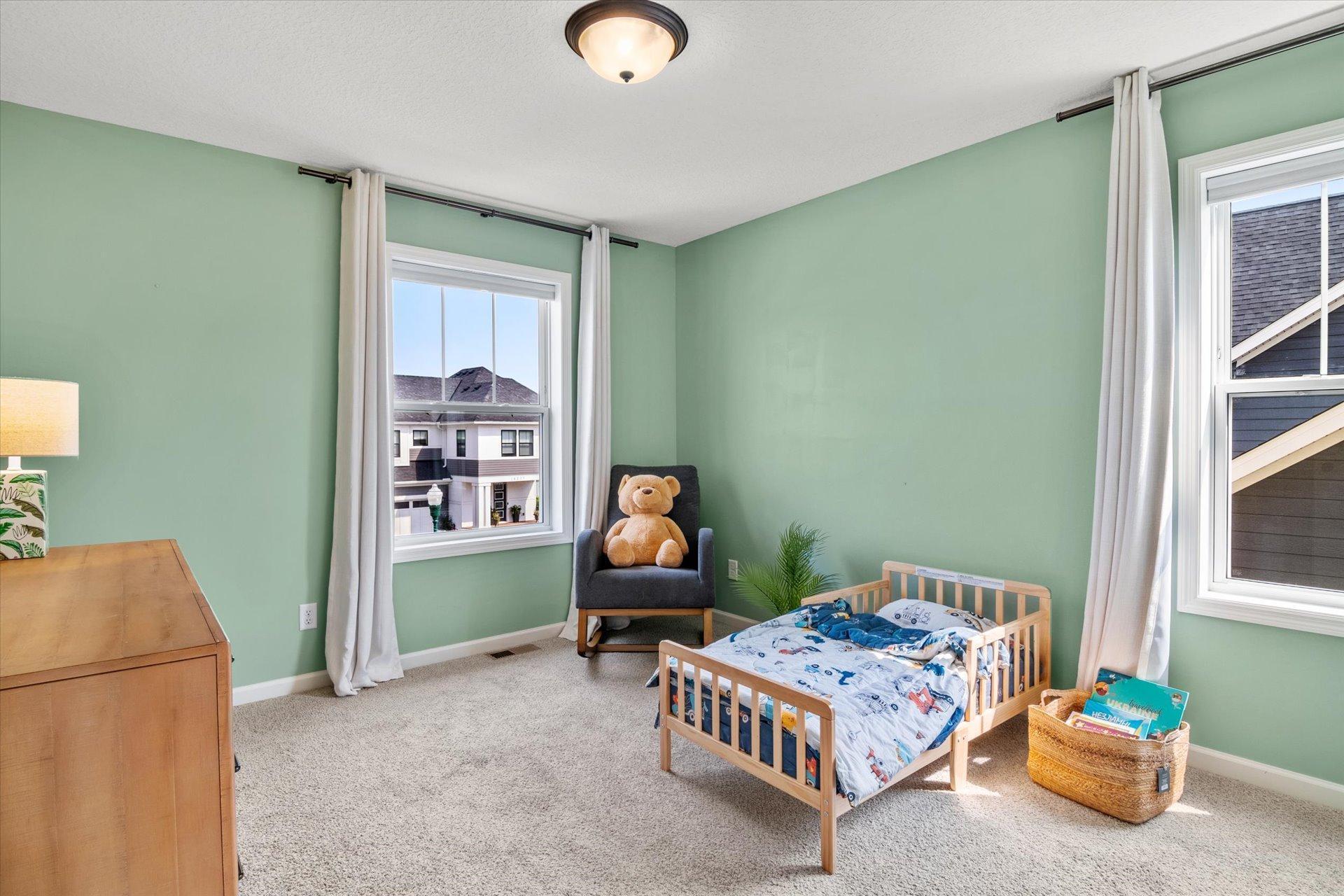 Bedroom with mint-green walls, a wooden crib, and an armchair holding a teddy bear.