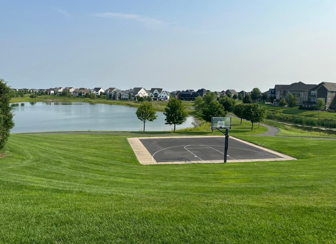 Neighborhood park with a basketball court beside a pond and walking path.