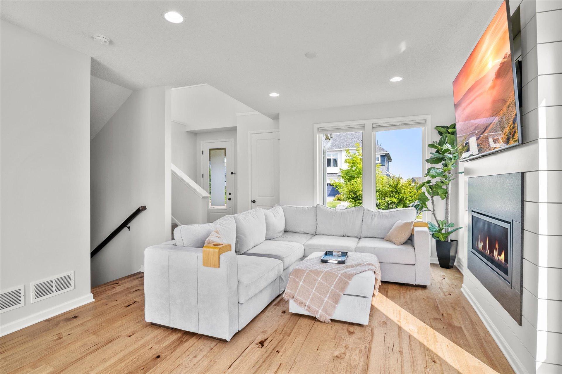 Living room with a white sectional, hardwood floors, and a modern fireplace beside large windows.