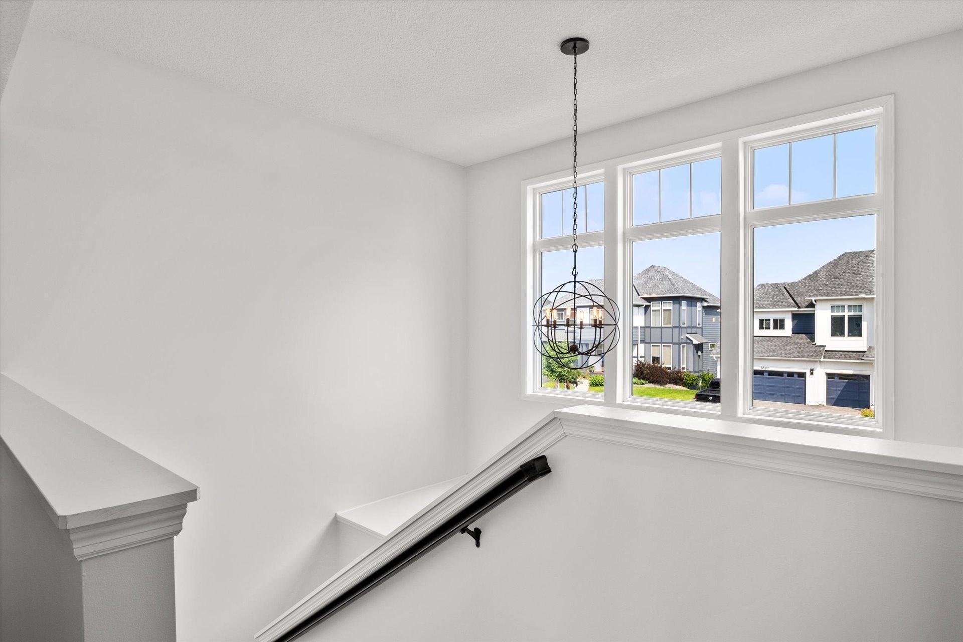 Upstairs stair landing with a spherical chandelier and tall windows overlooking neighboring homes.