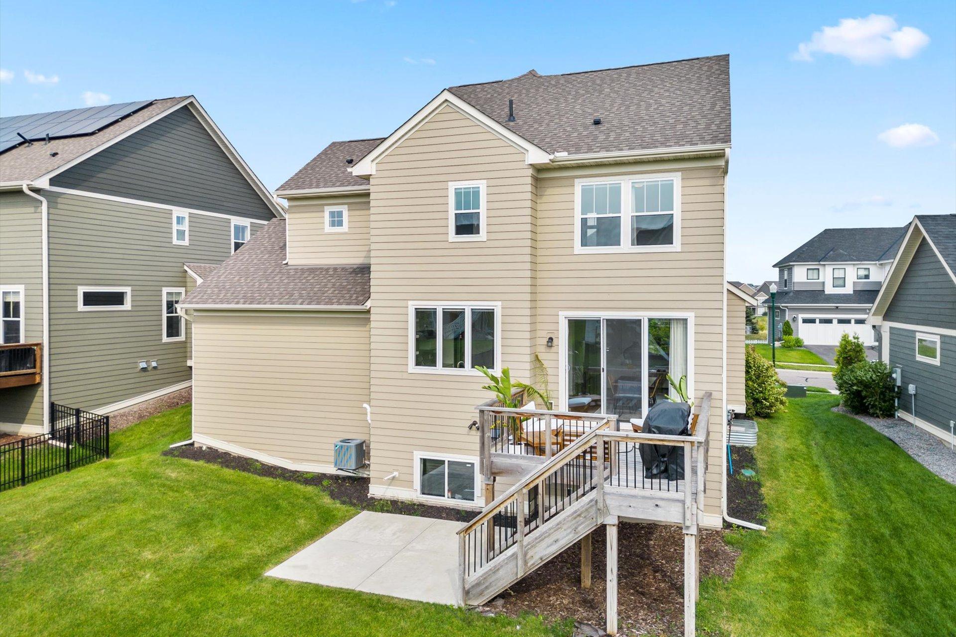 Rear of a beige two-story home with a raised deck, long wooden ramp, and green lawn.