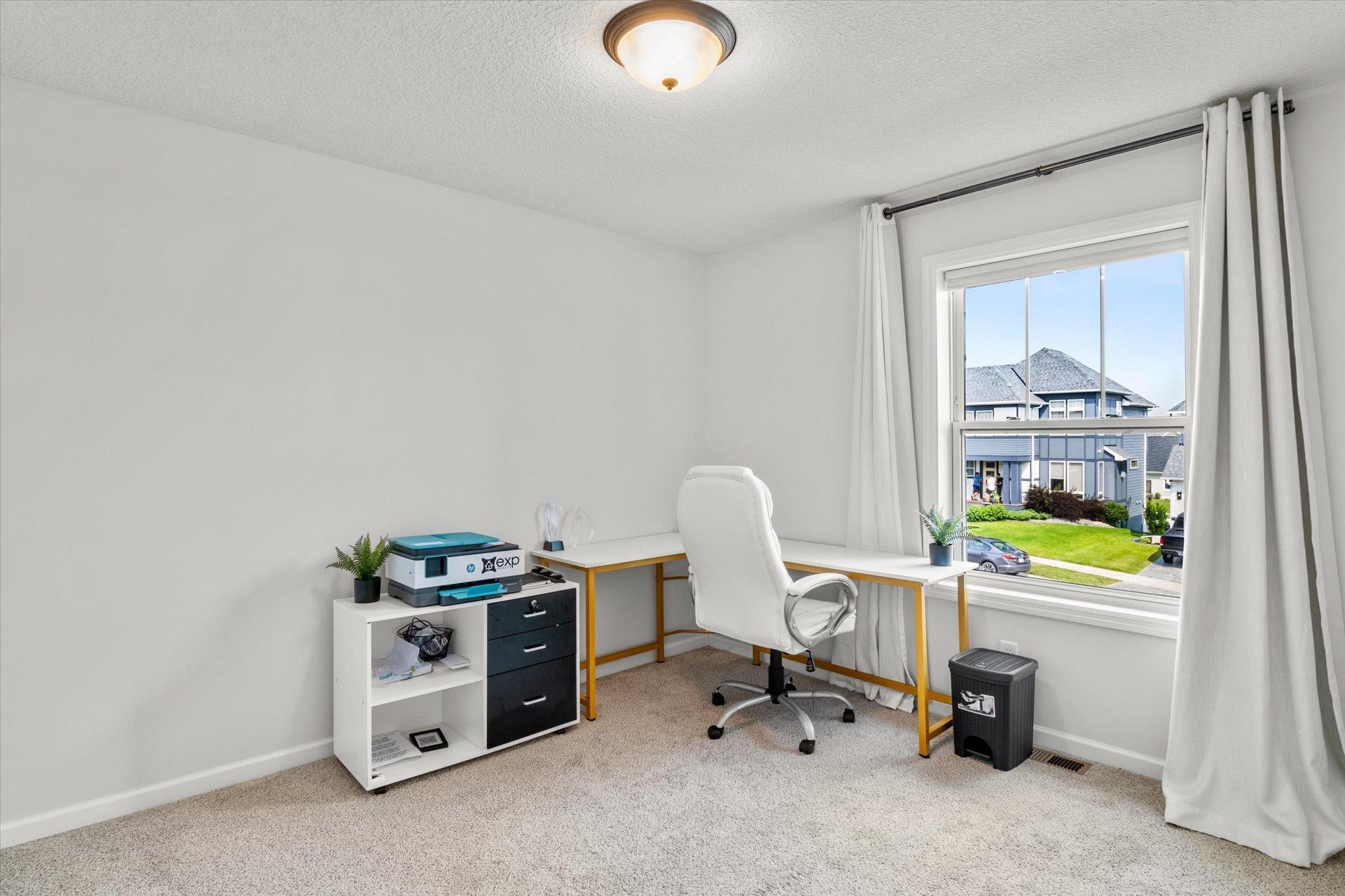 Home office with a white desk and chair beside a large window overlooking neighboring homes.