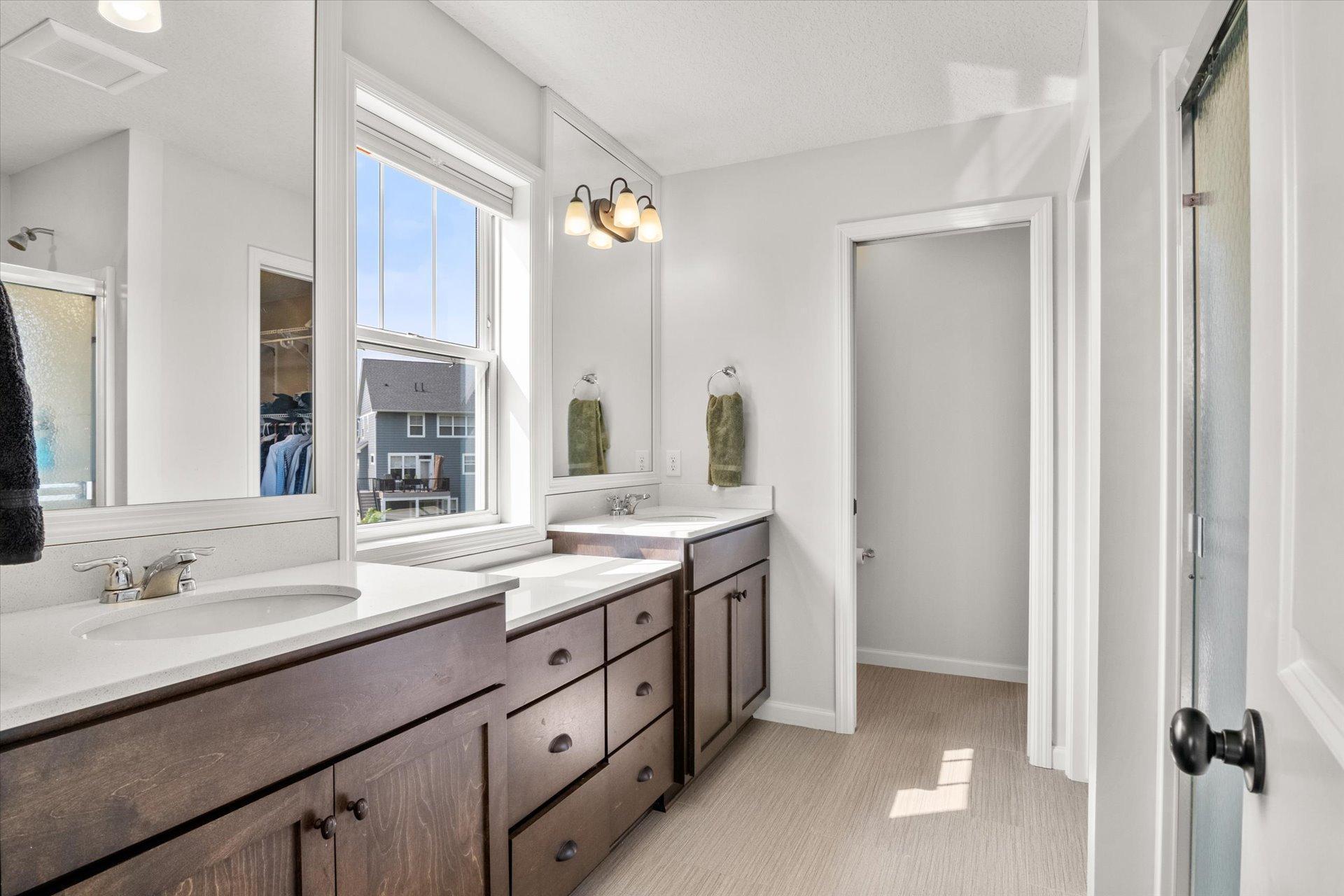 Bathroom with a dark wood double vanity, two sinks, large mirrors, and a sunny window.