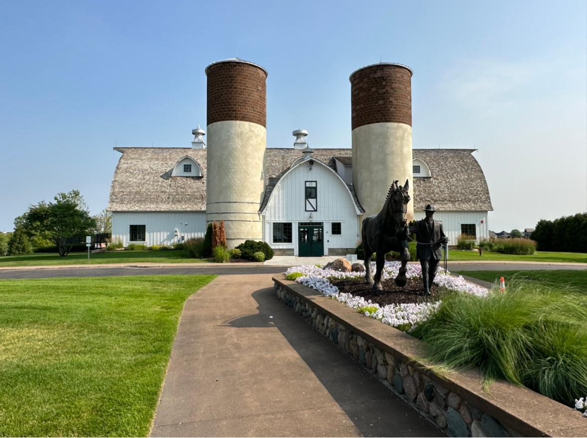 White barn-style building with twin silos behind a flower bed and horse-and-rider statue.