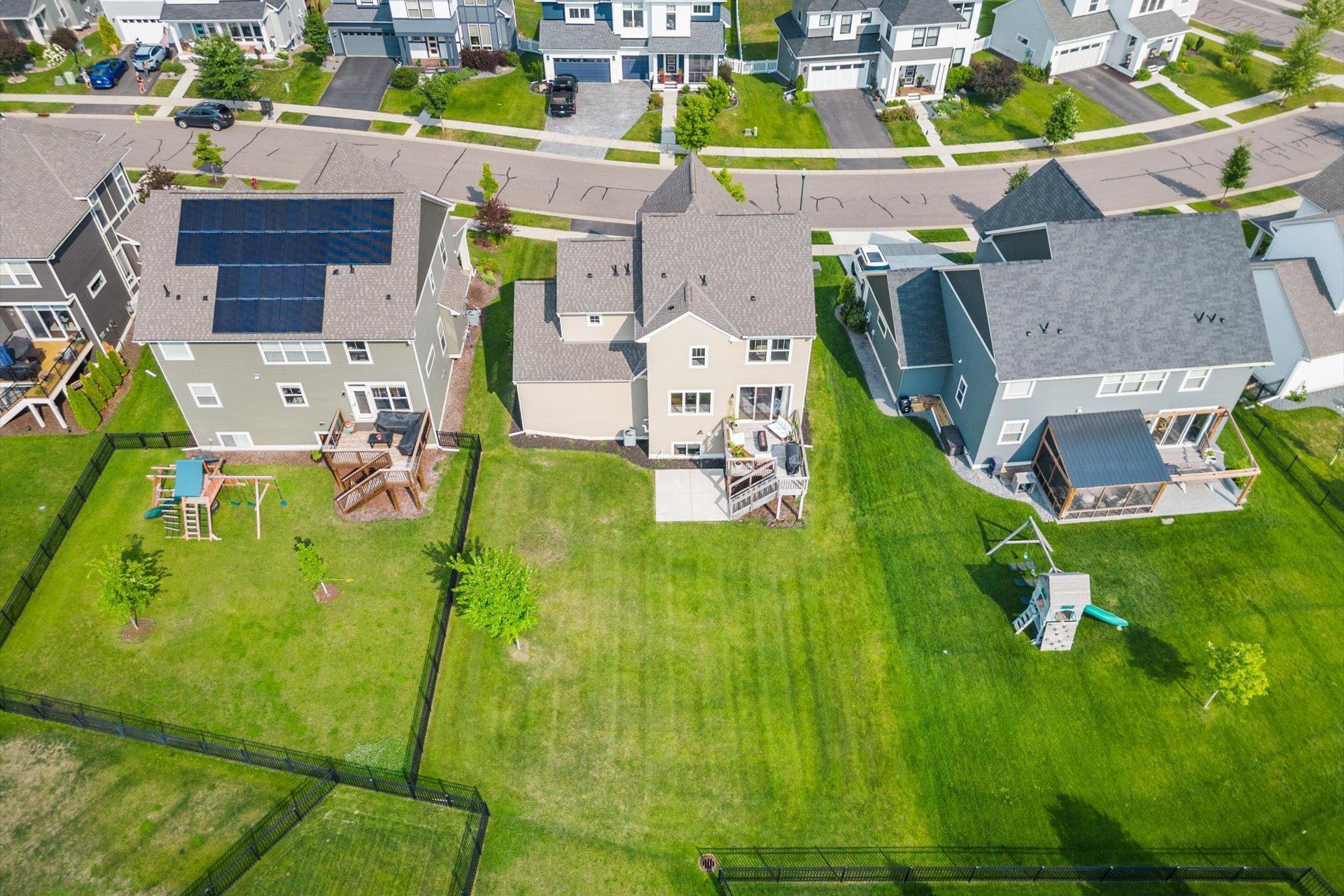 Aerial view of a home’s fenced backyard, with a broad lawn and neighboring houses.