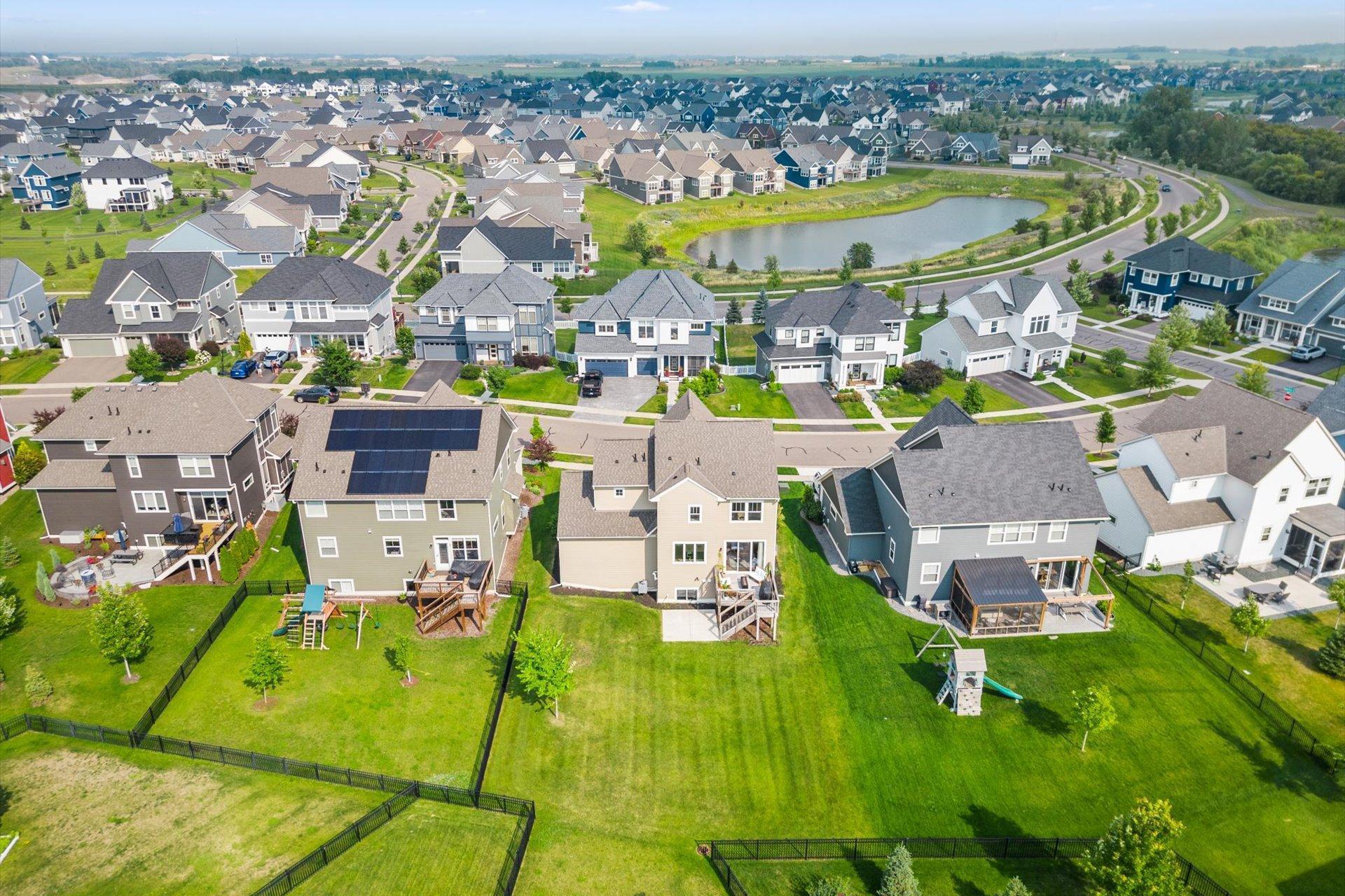 Aerial view of a Lakeville neighborhood with a pond, curving road, and fenced backyards.