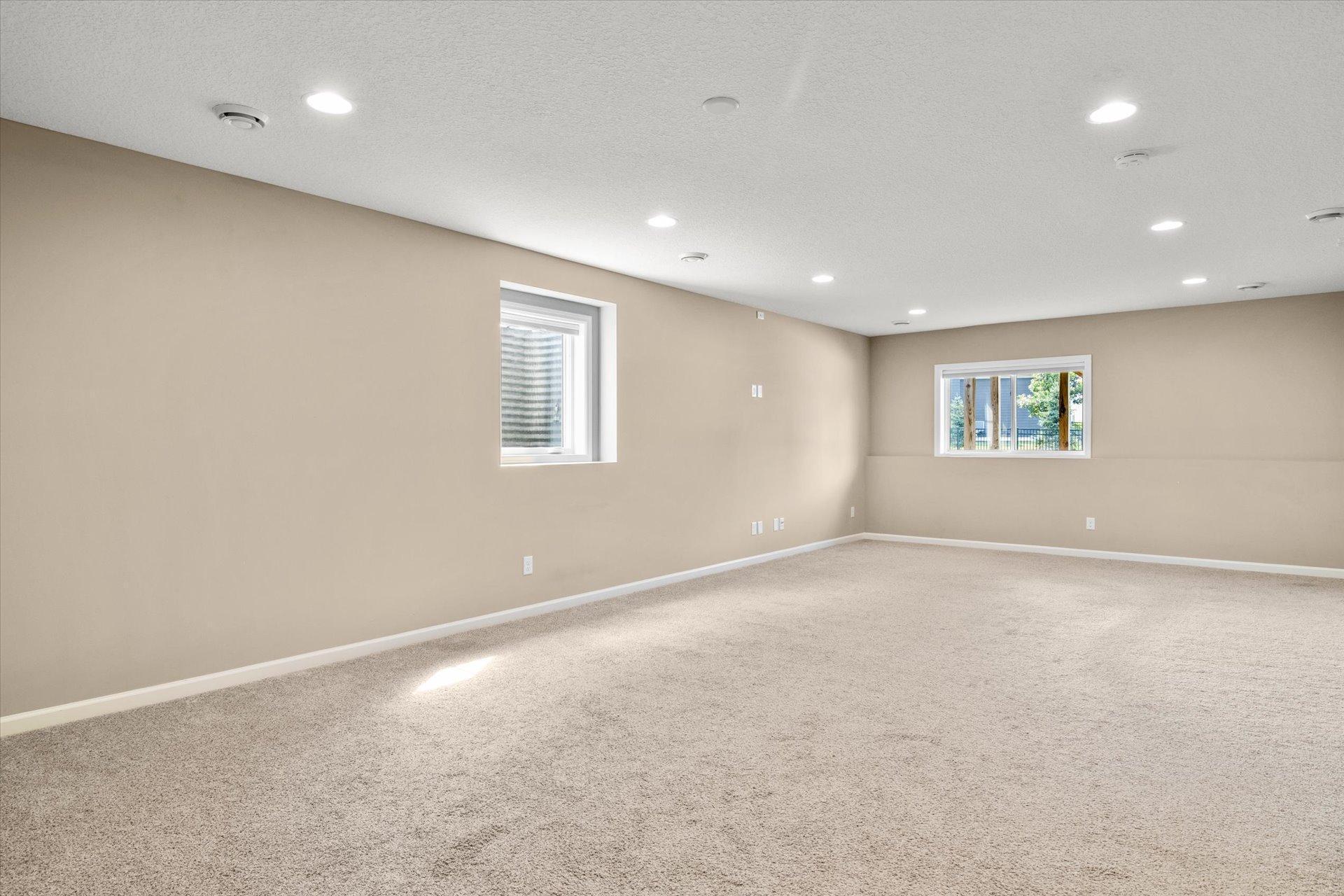 Empty carpeted room with beige walls, recessed lights, and two windows.