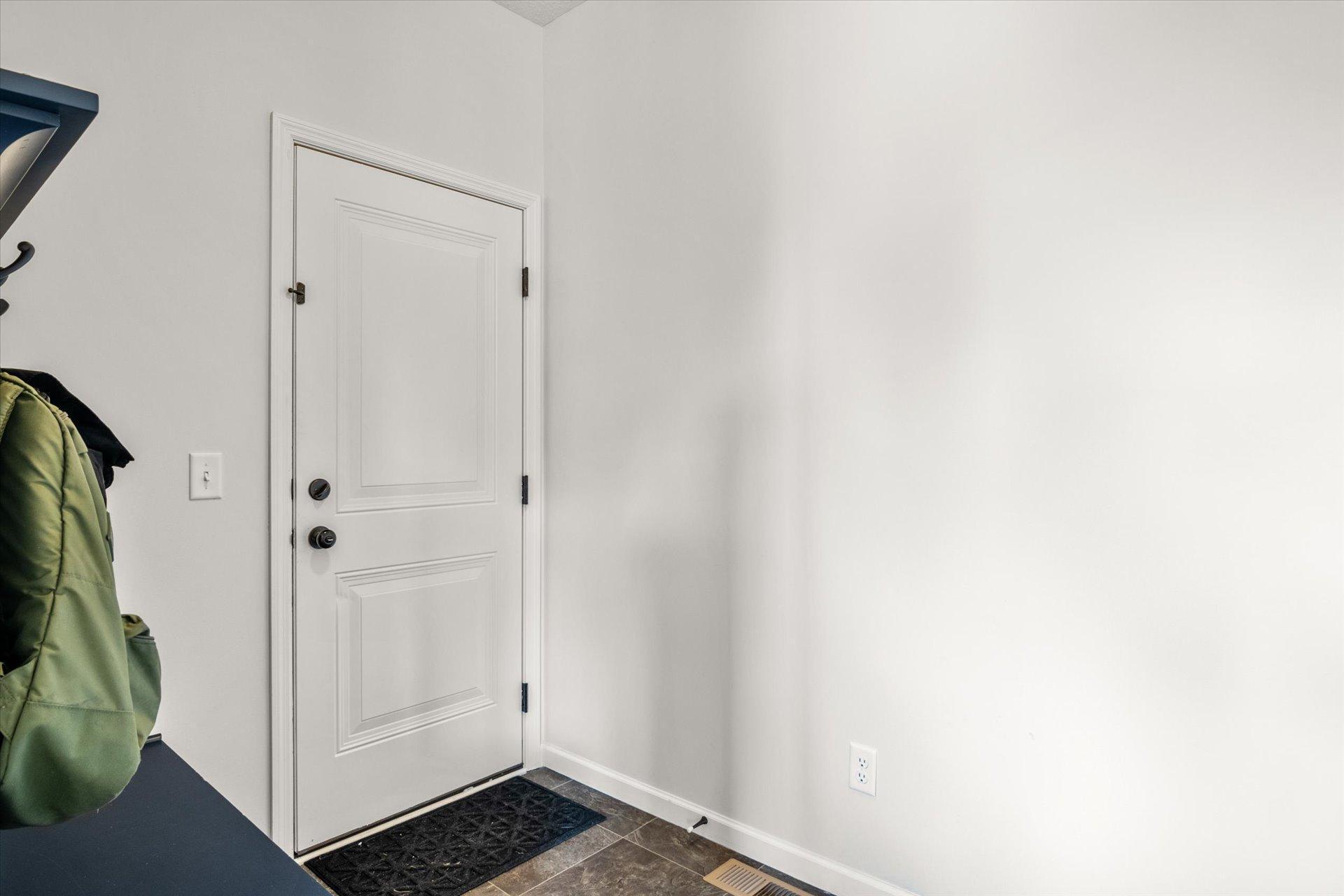 Entryway with a white paneled front door, tiled floor, and coats on a wall rack.