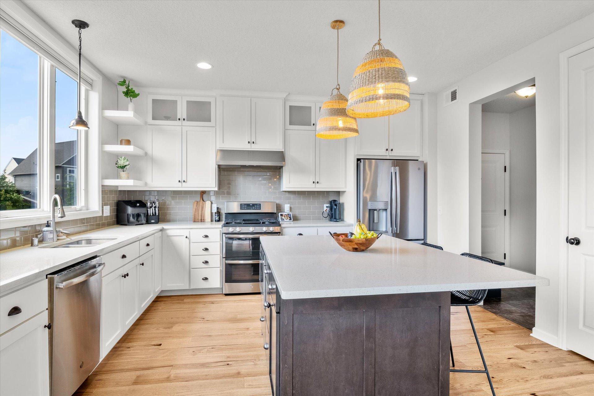 Bright kitchen with white cabinets, stainless steel appliances, and a large island beneath woven pendant lights.