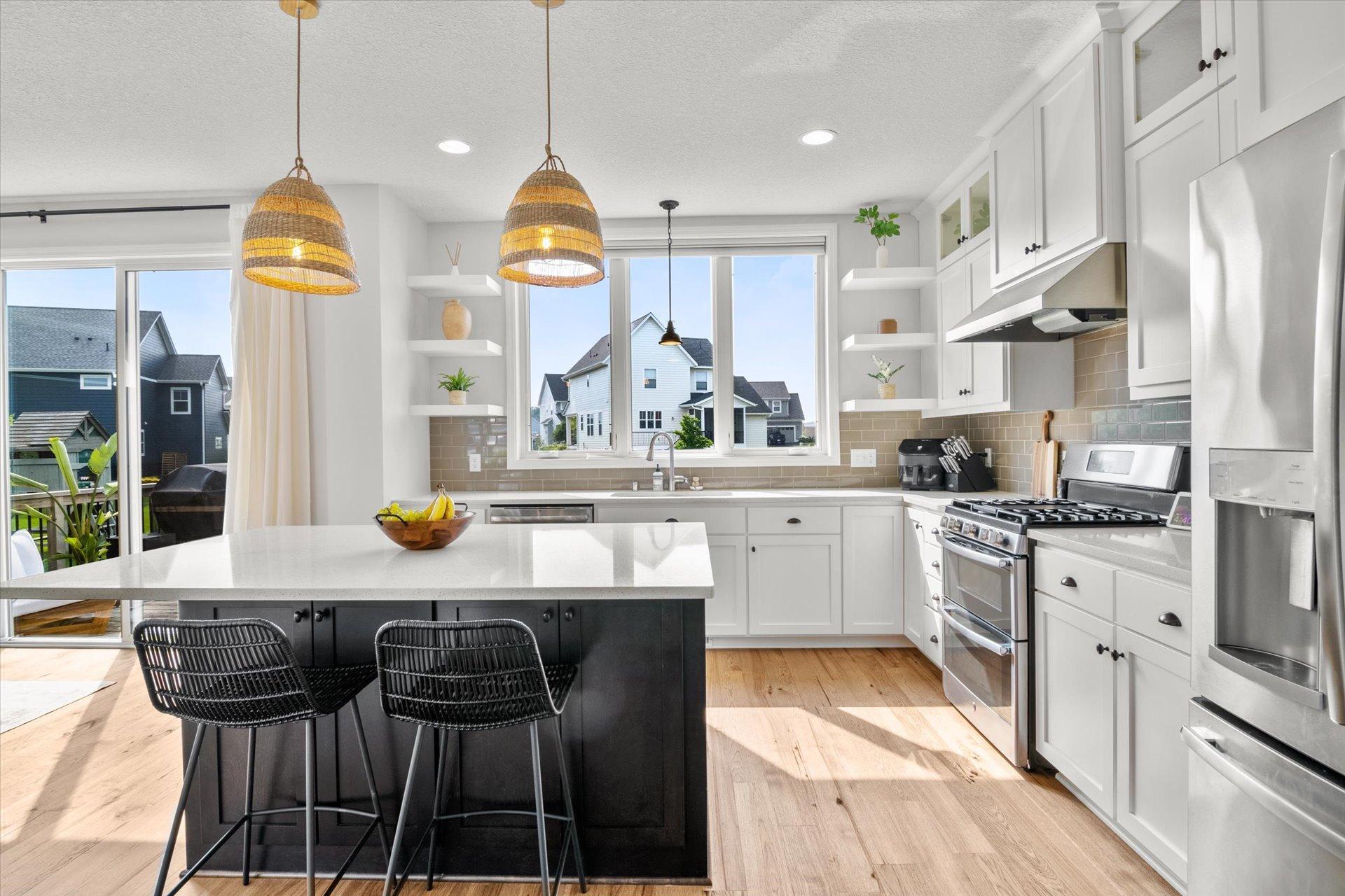 Bright kitchen with a dark island, white cabinets, woven pendant lights, and large windows.