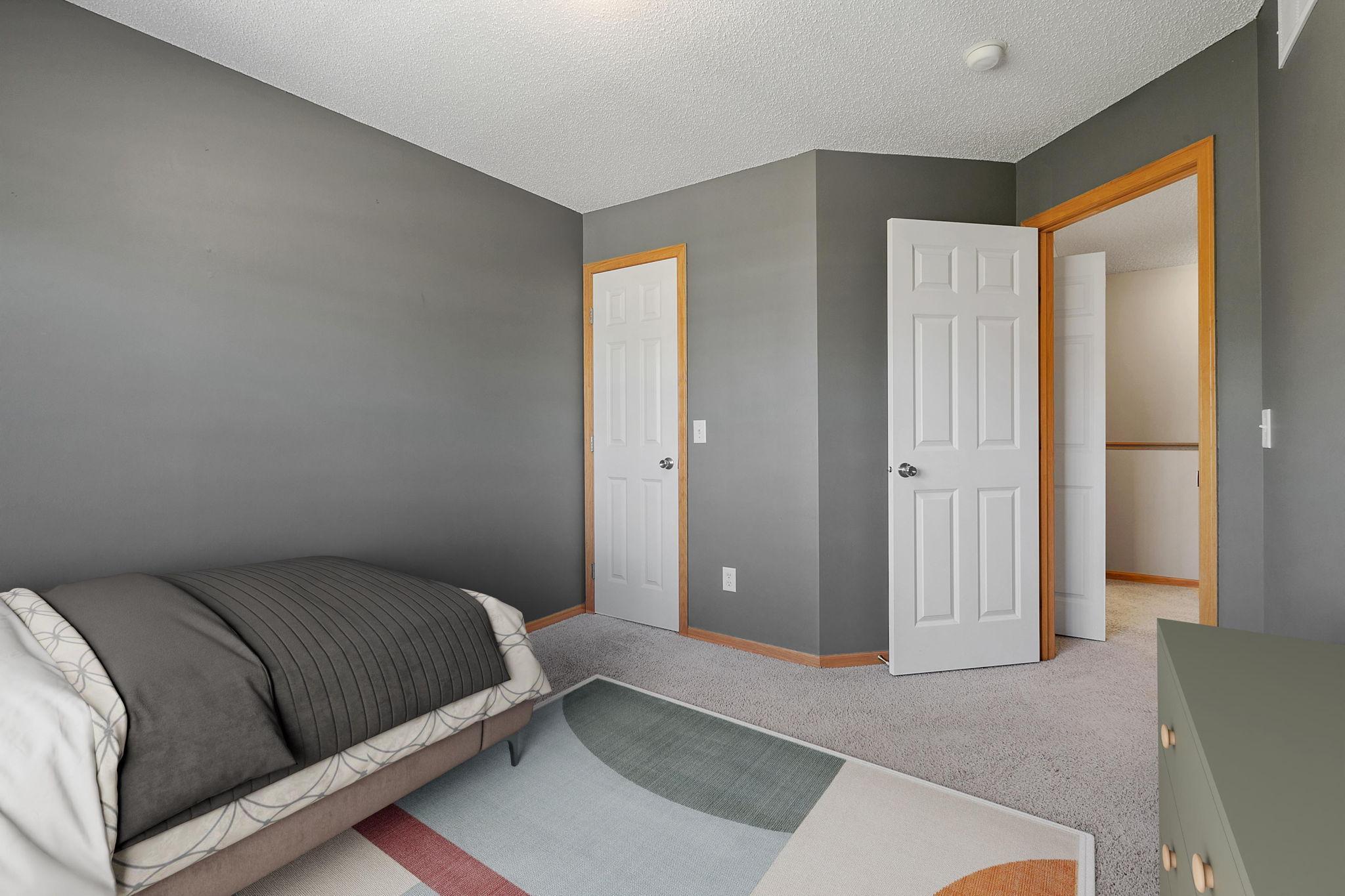 Bedroom with gray walls, a bed with gray bedding, geometric rug, and open closet doorway.
