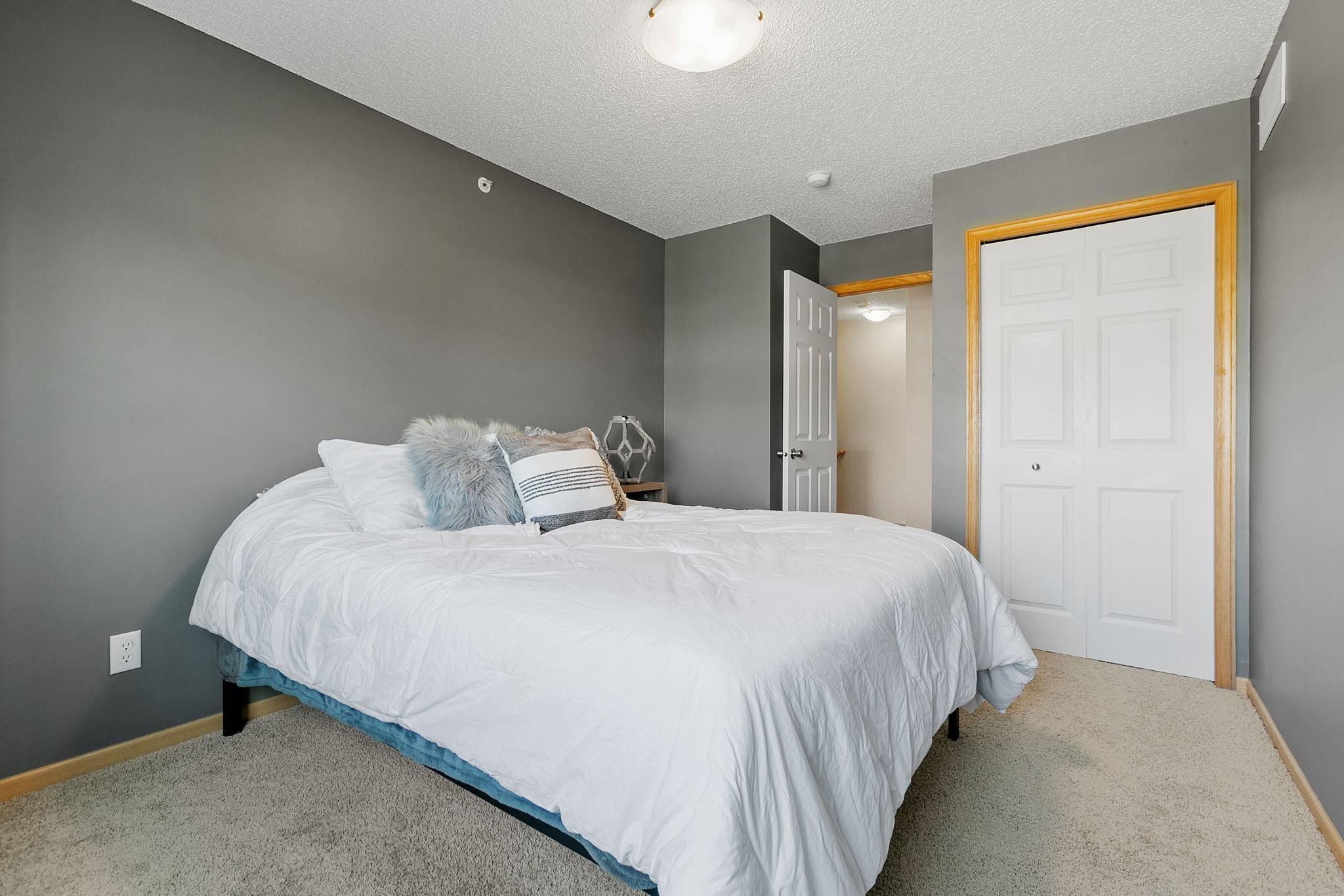 Bedroom with a white-covered bed, gray walls, beige carpet, and wood-trimmed closet doors.