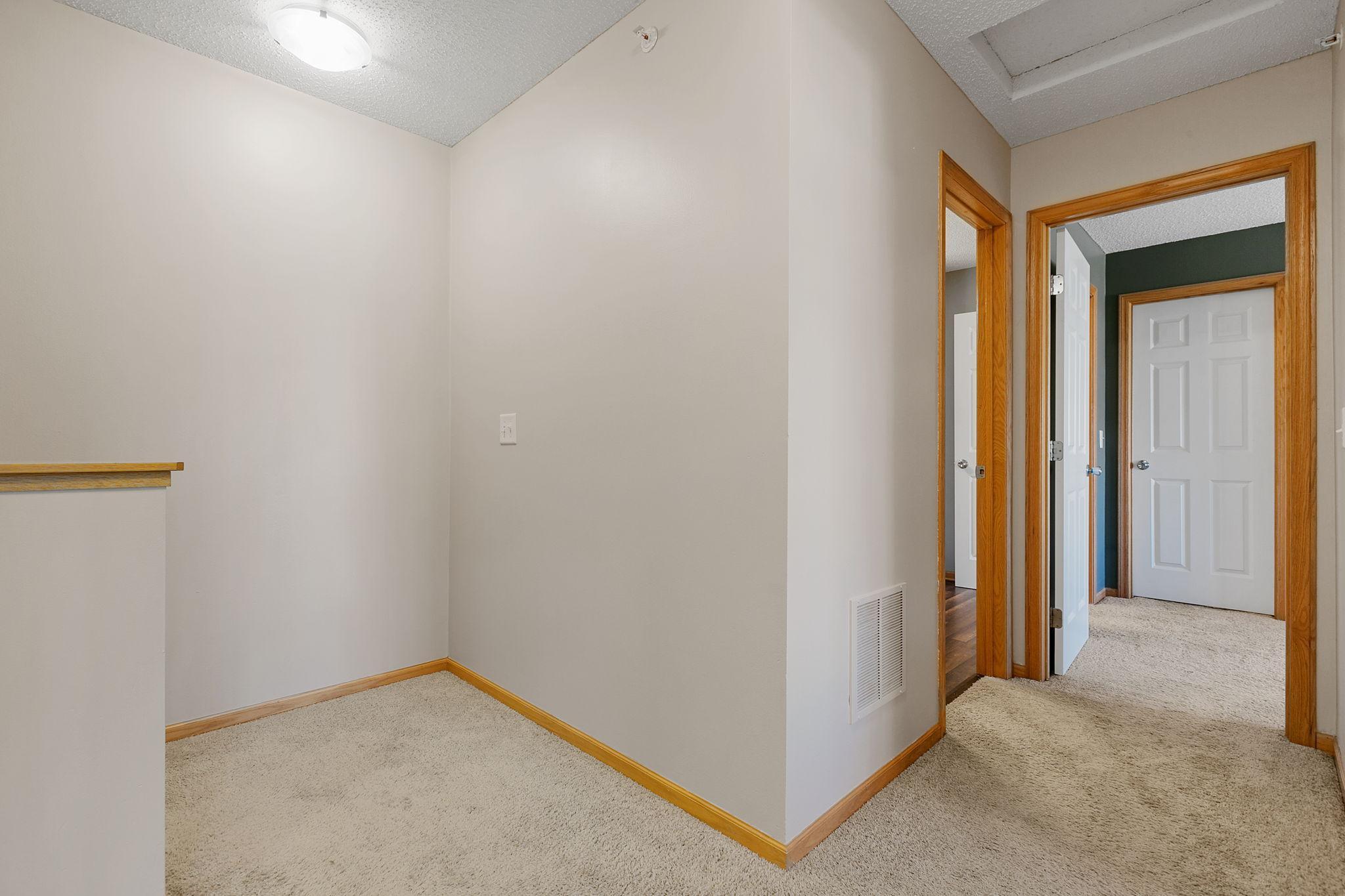 Carpeted upstairs hallway with warm wood trim and several open doorways.