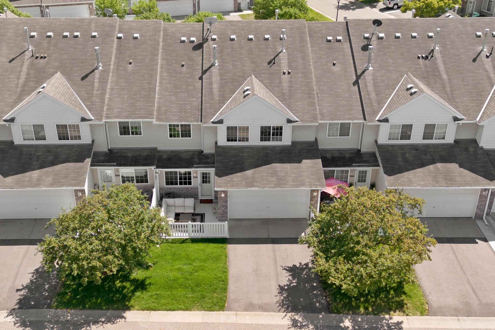 Aerial view of attached townhomes, with the featured unit’s patio, lawn, and garage visible.
