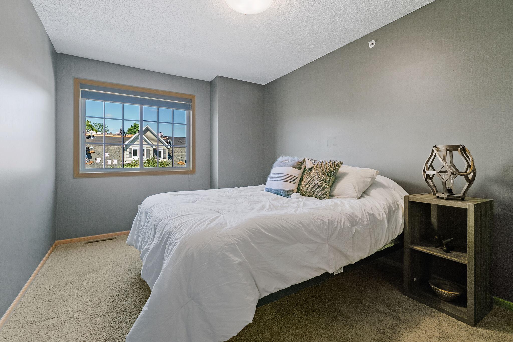 Bedroom with a white bed and a window overlooking a neighboring house.