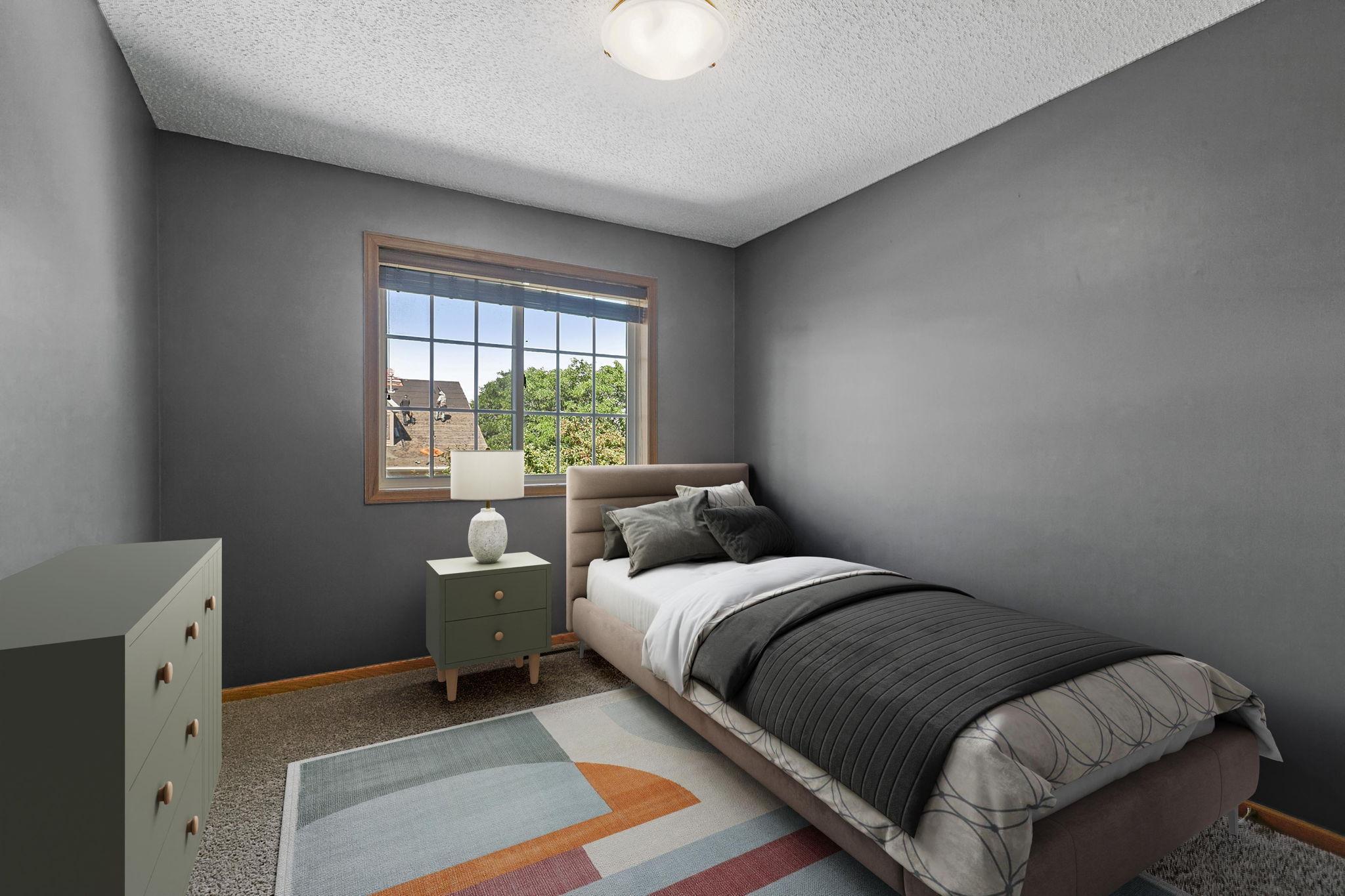 Furnished bedroom with gray walls, a charcoal-covered bed, and a window overlooking leafy trees.