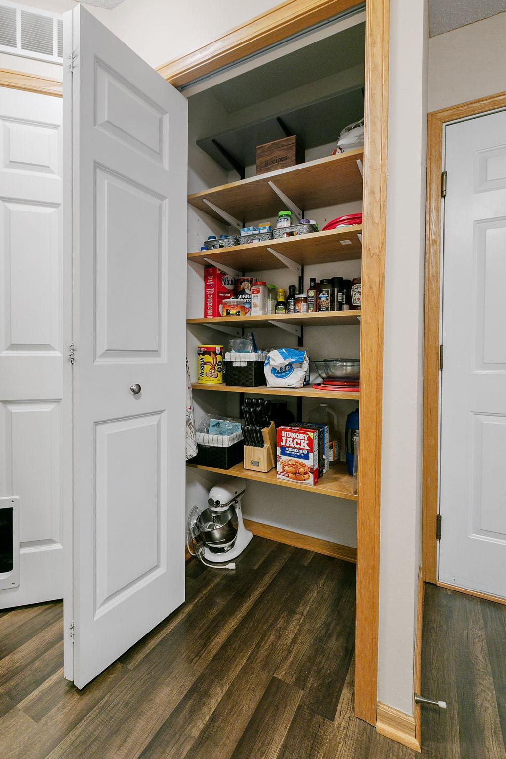 Walk-in pantry with stocked wooden shelves and a stand mixer on the floor.