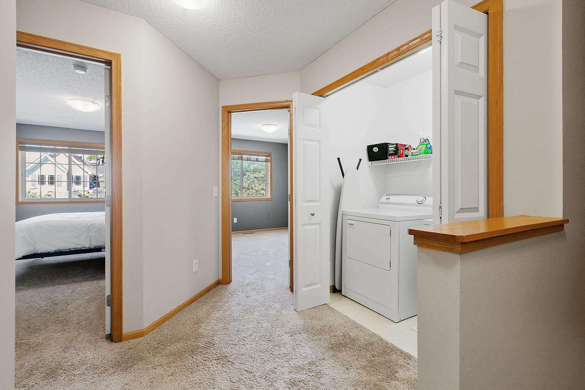 Laundry closet with a white washer and dryer beside bedroom doorways and a wood counter ledge.