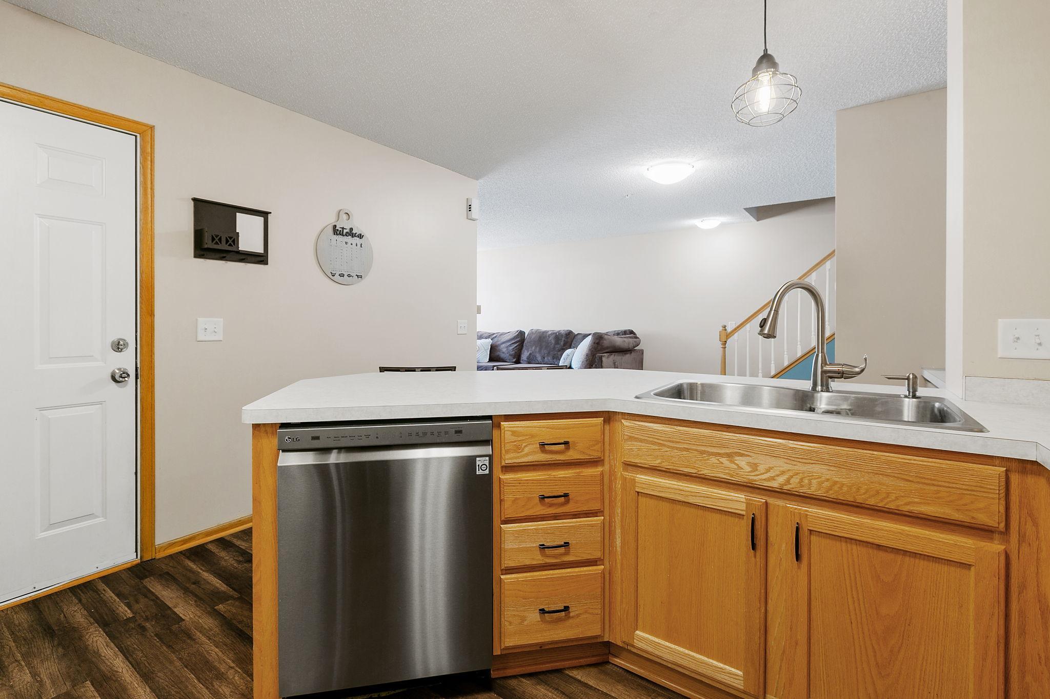 Kitchen with honey-oak cabinets, a peninsula sink, stainless-steel dishwasher, and adjoining living area.