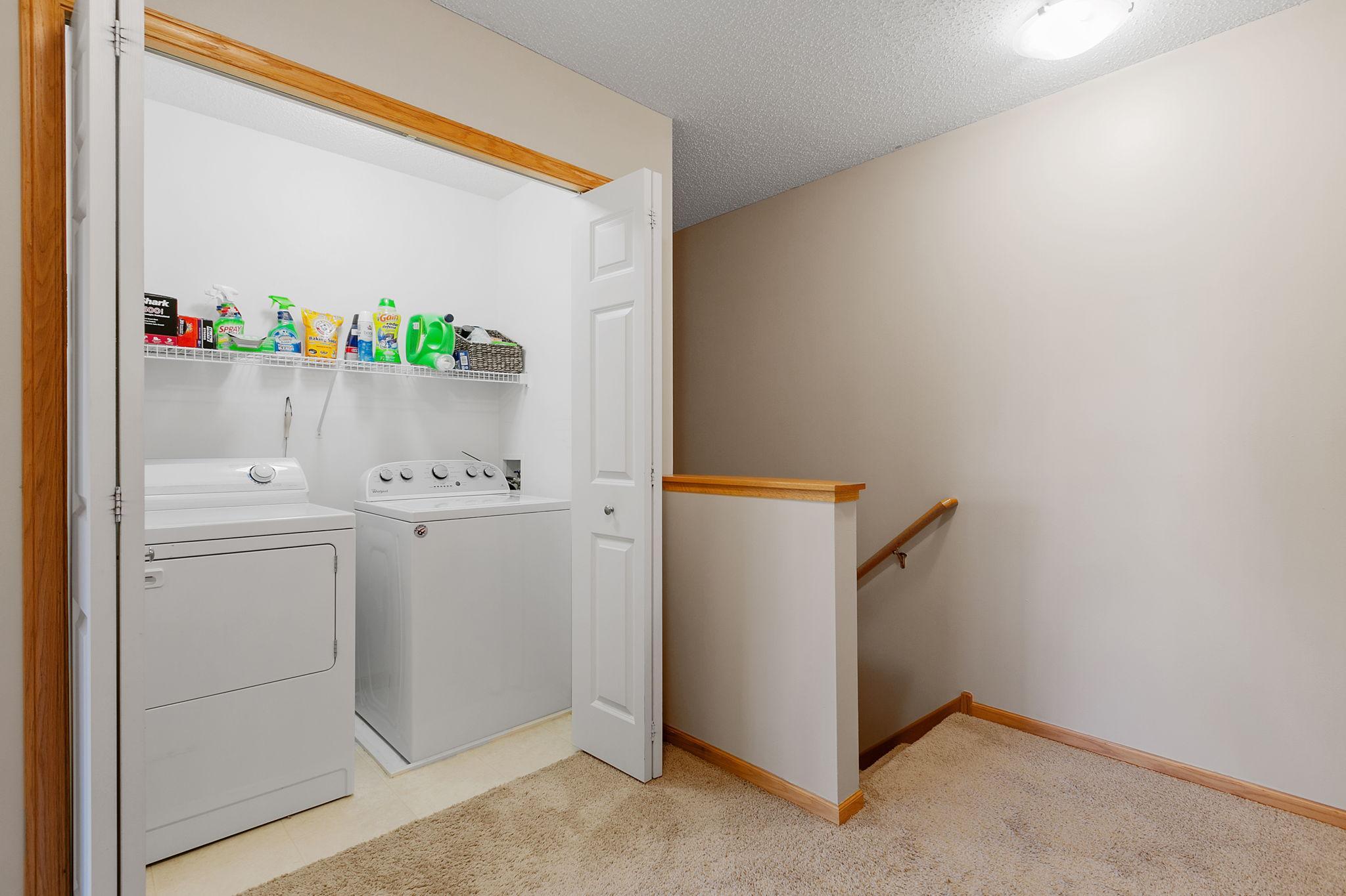 Laundry closet with washer, dryer, and cleaning supplies beside a carpeted stair landing.