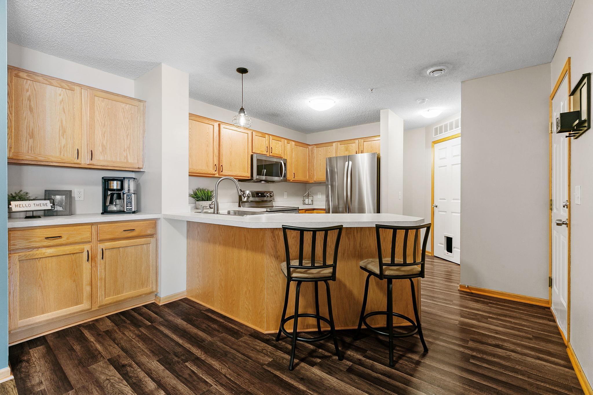 Kitchen with light wood cabinets, stainless steel appliances, and a peninsula with two bar stools.