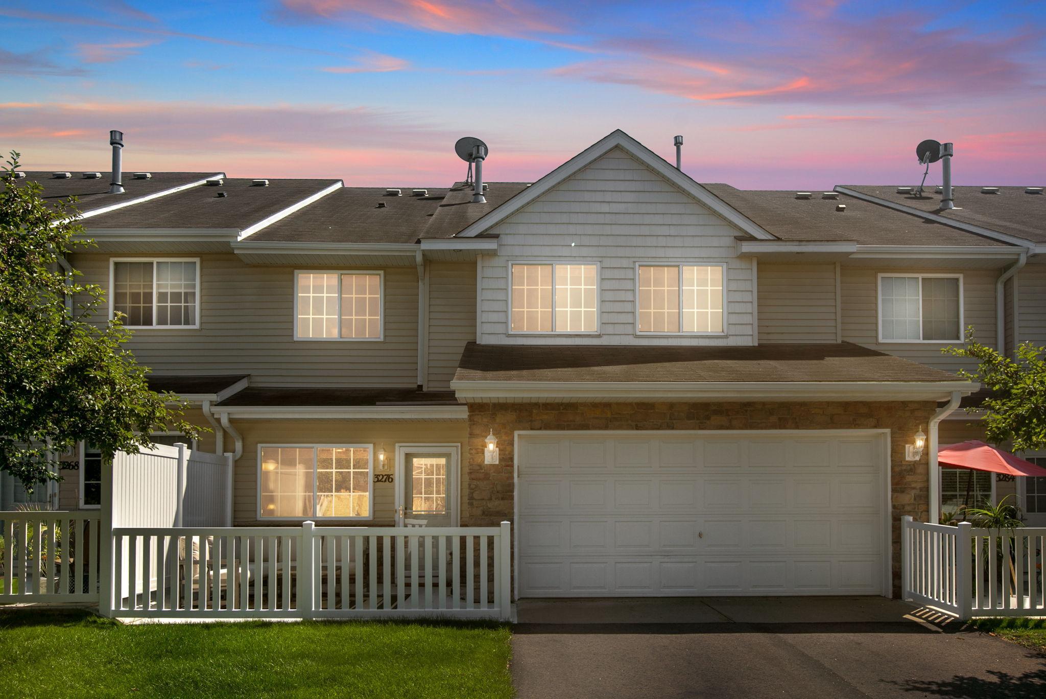 Two-story attached home with a stone-faced garage and white entry fence at dusk.