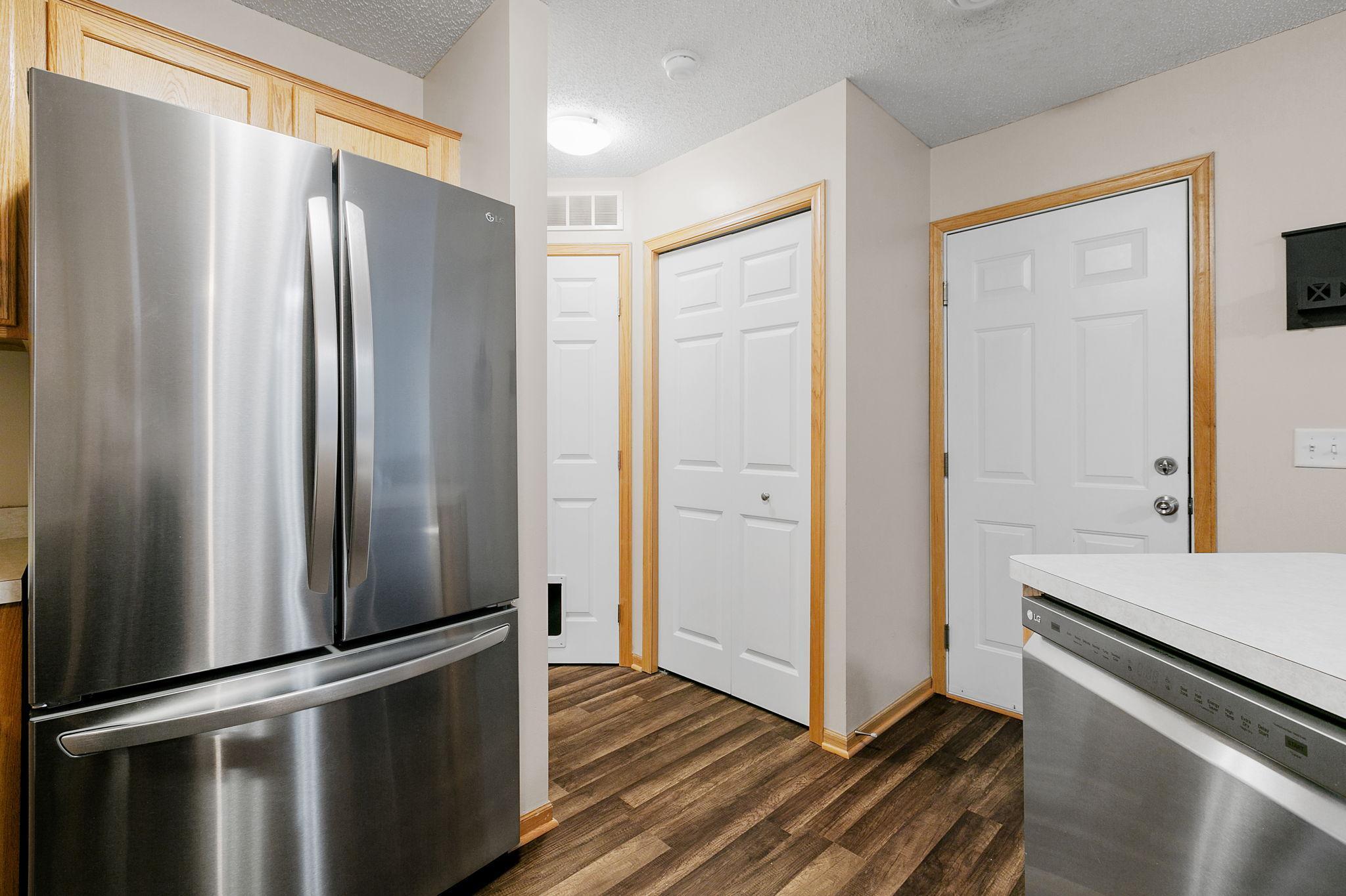 Kitchen with stainless-steel appliances, light wood cabinets, white countertops, and dark flooring.