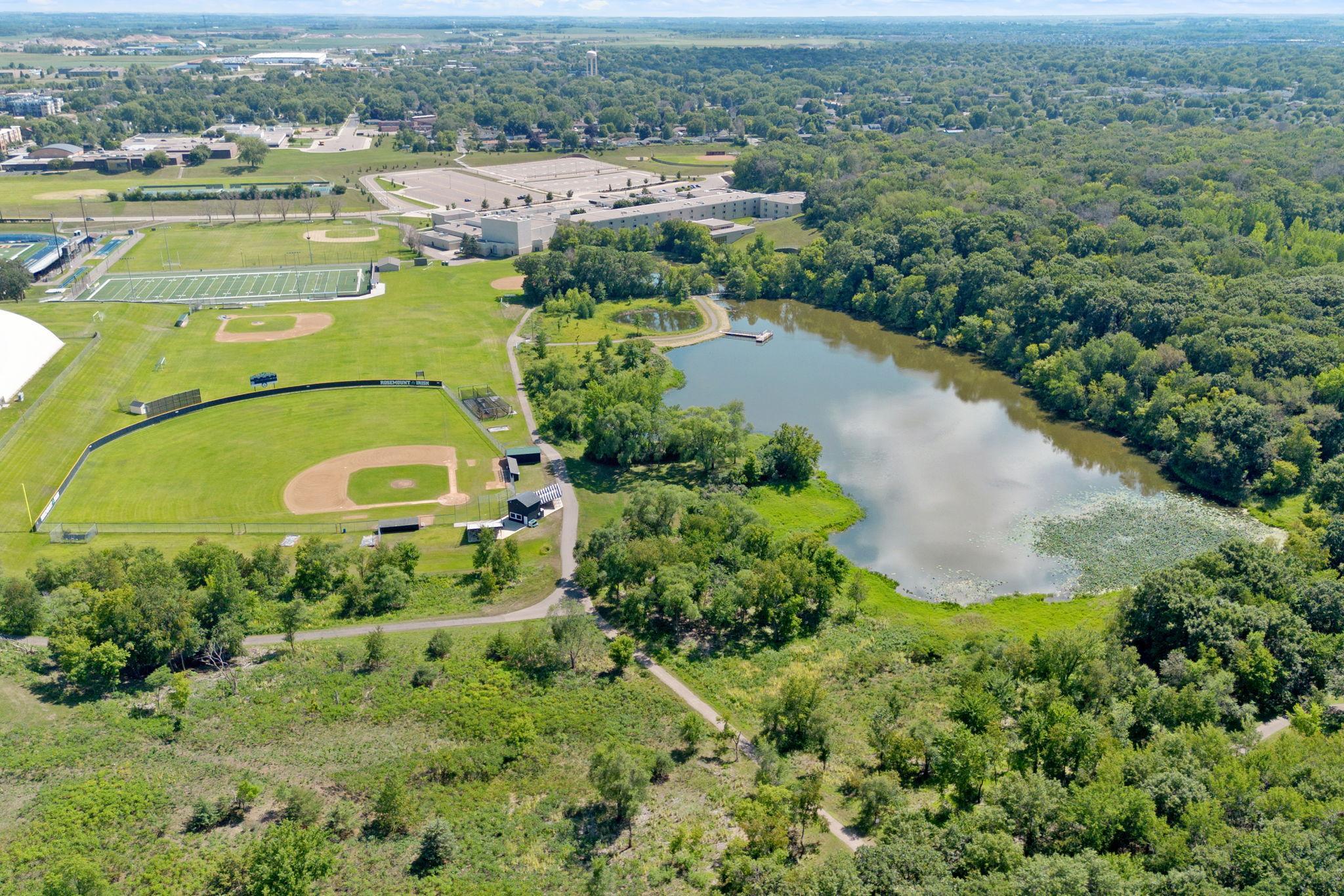 Aerial view of a lake beside wooded trails and a sports complex with baseball and football fields.