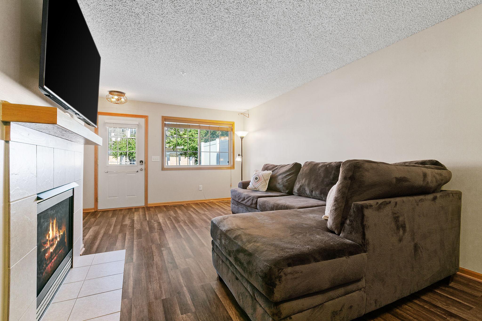 Living room with a dark sectional sofa, tiled fireplace, and wood-look flooring.
