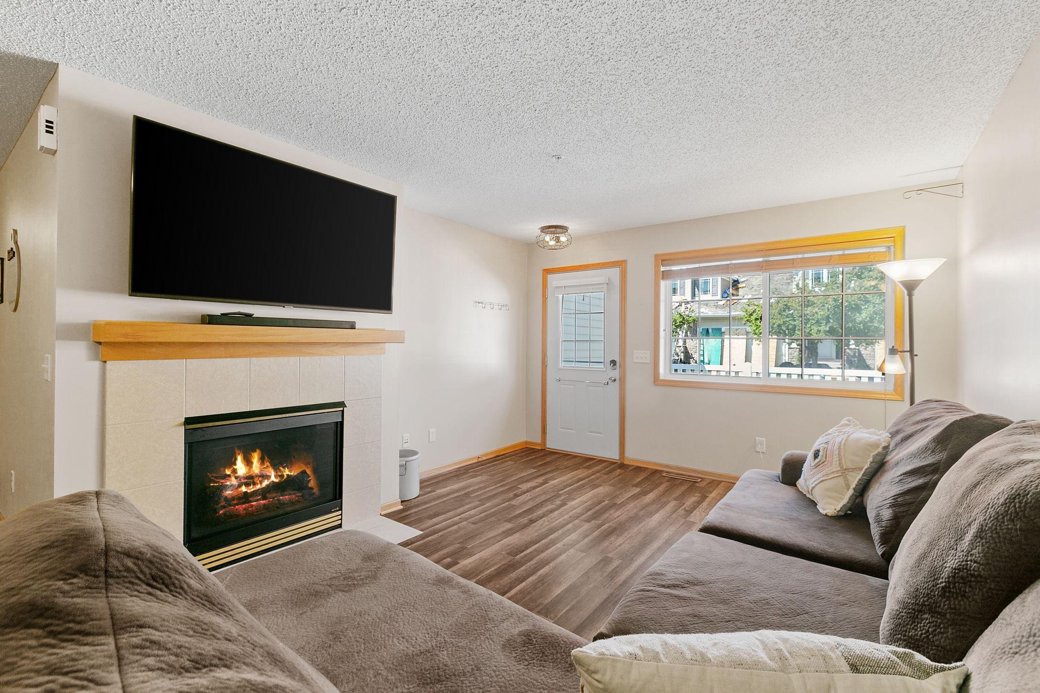 Living room with a tiled fireplace, large TV, brown sofas, and a wide window.
