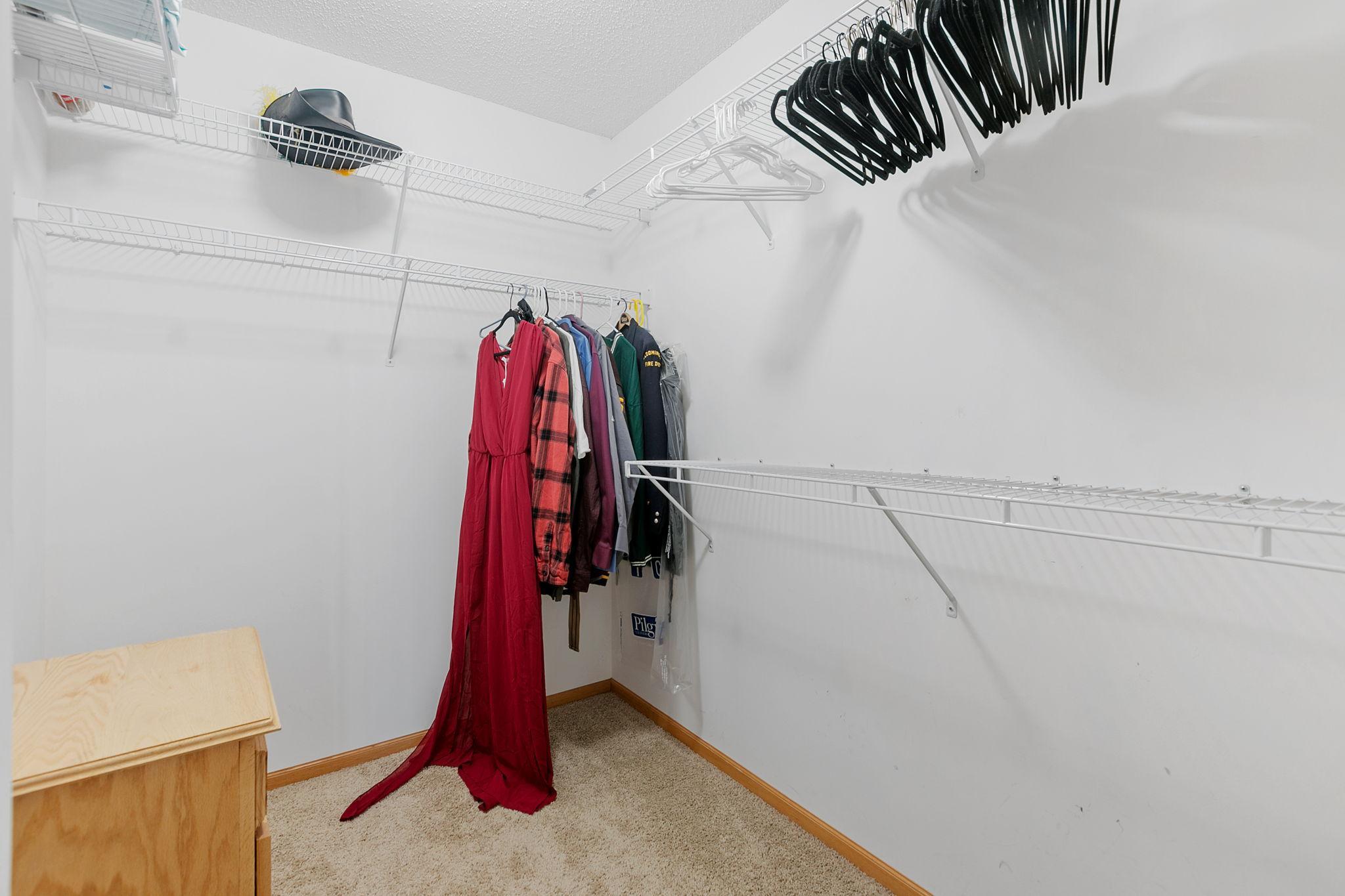 Walk-in closet with white wire shelving, hanging clothes, and a long red dress.