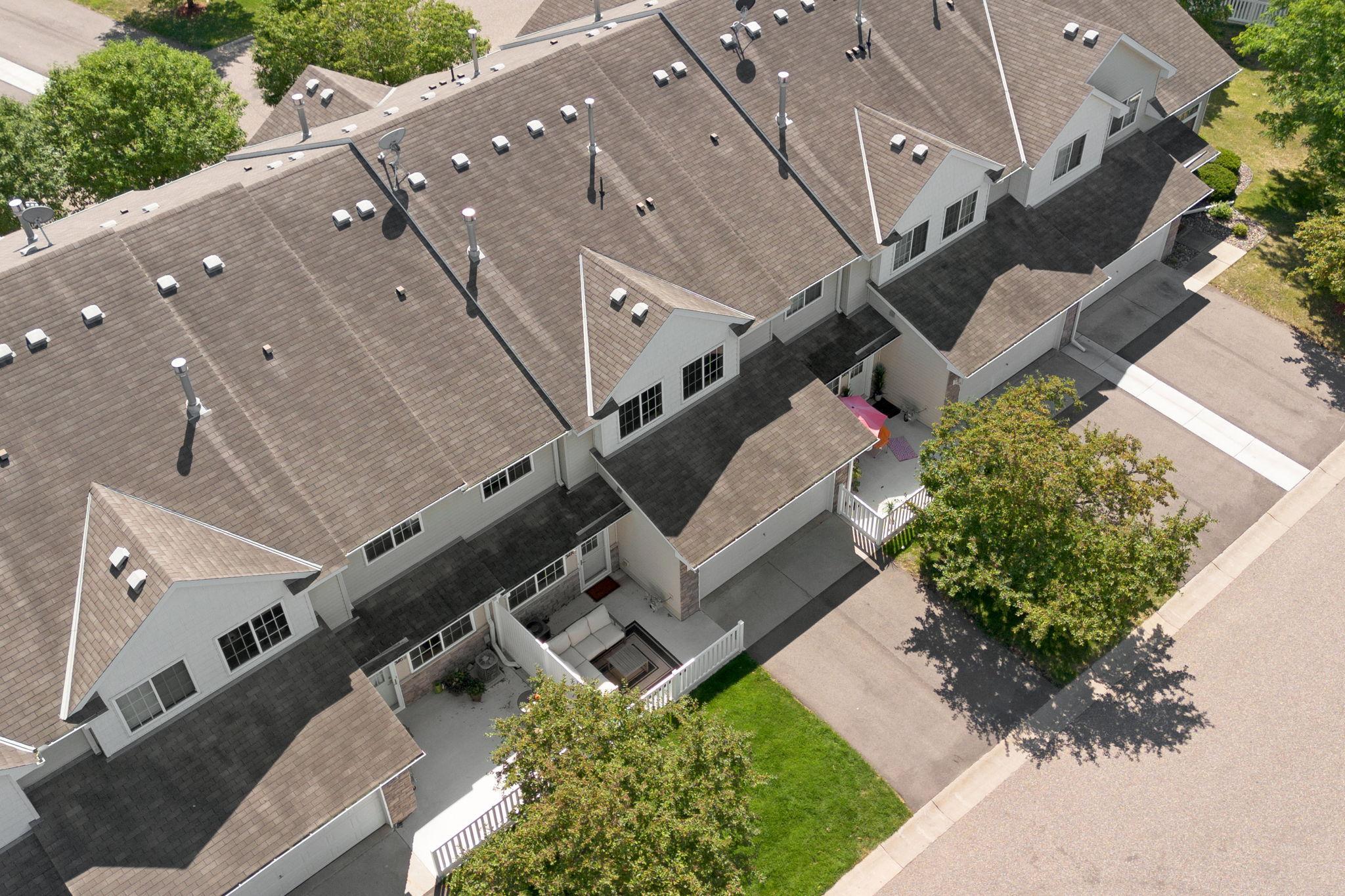 Aerial view of attached townhomes with gabled roofs, fenced patios, and a tree-lined drive.