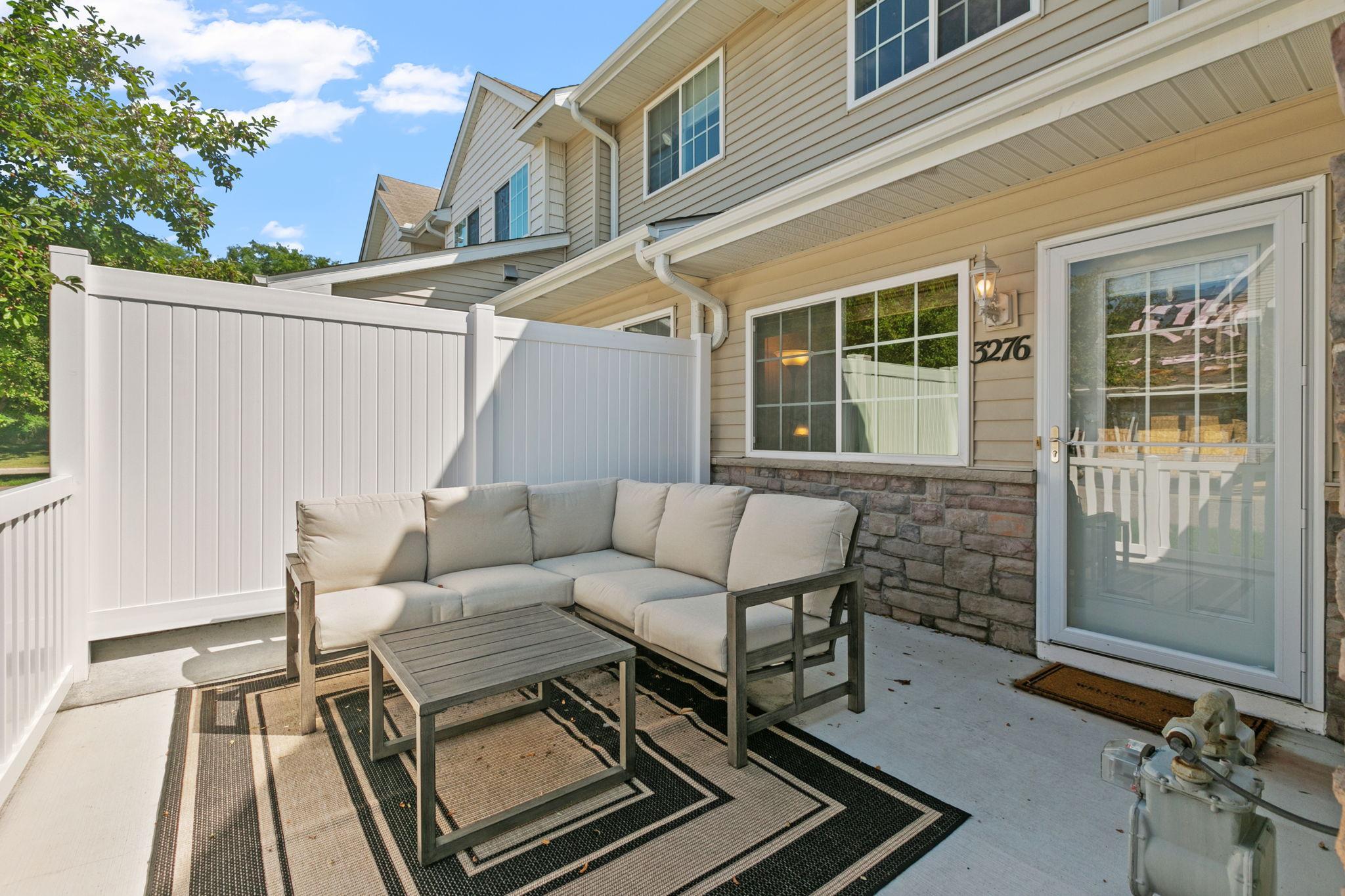 Townhouse patio with white privacy fencing and a cushioned sectional beside the glass door.