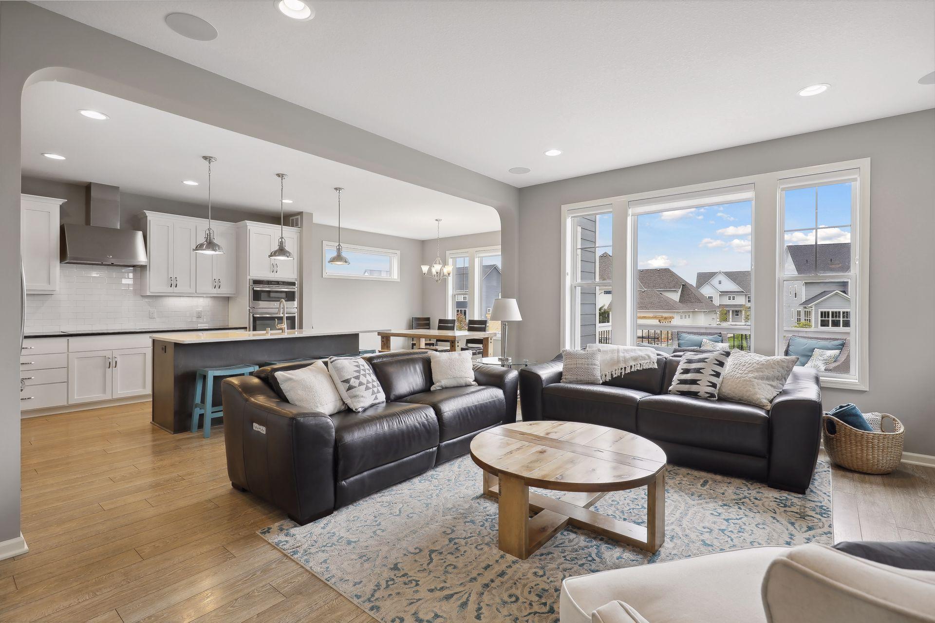 Open-plan living room and kitchen with black leather sofas, white cabinetry, and large windows.