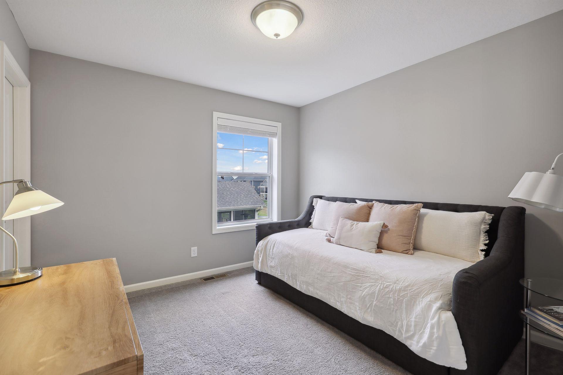 Bedroom with a dark upholstered daybed, soft neutral pillows, and a window overlooking neighboring homes.