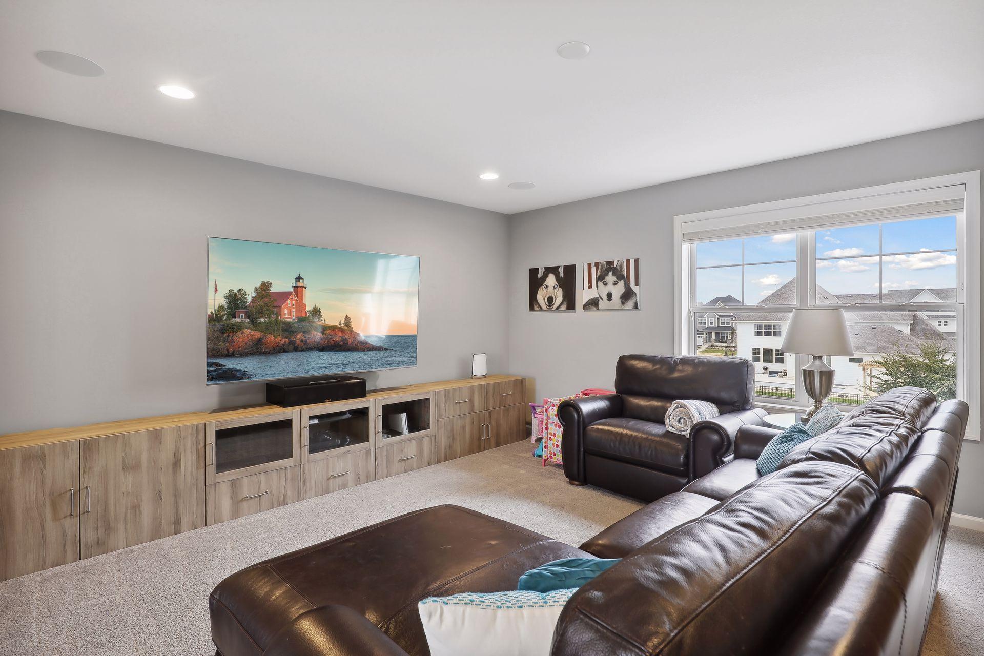 Furnished living room with a leather sectional, media cabinetry, wall-mounted television, and a large window.