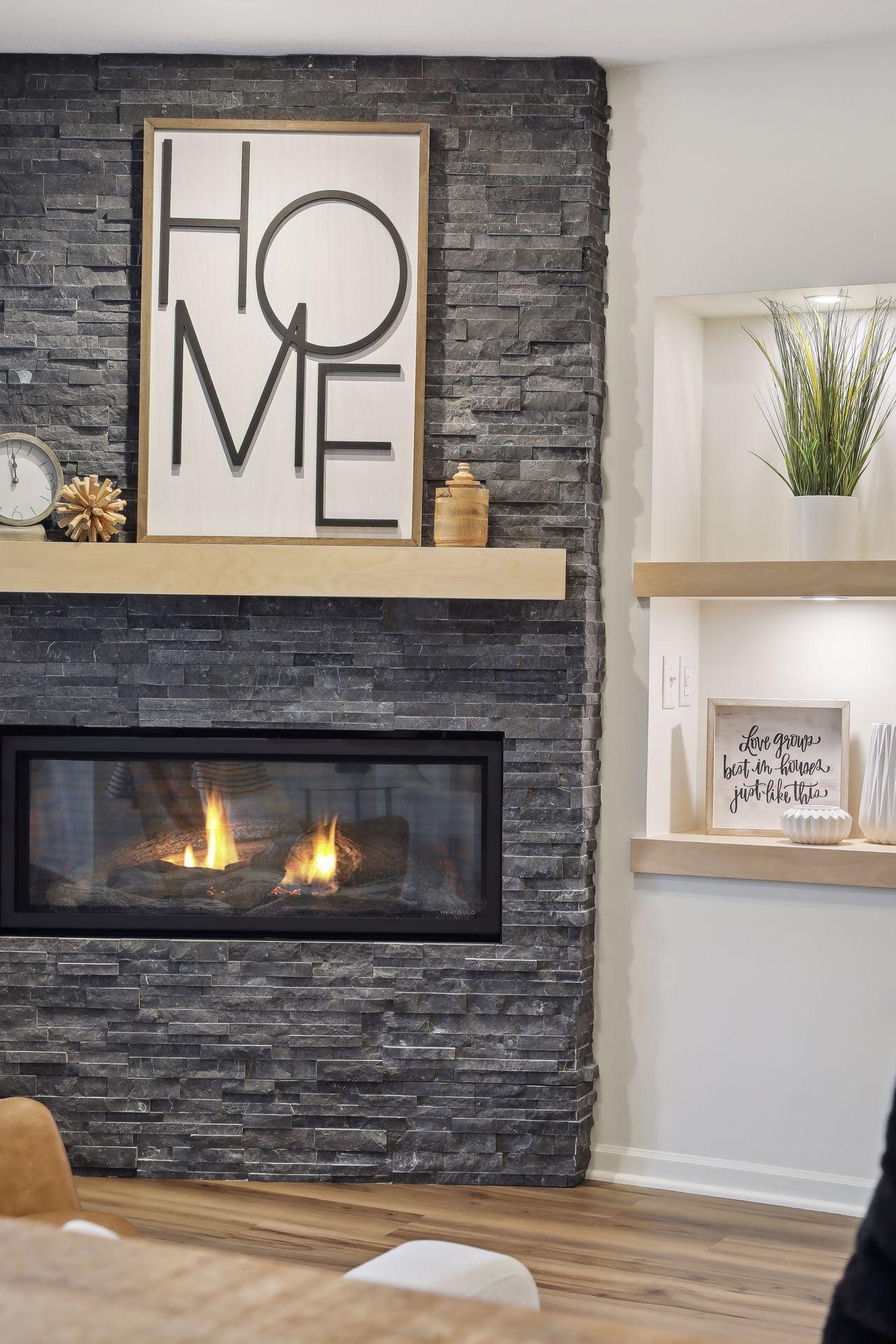 Living room fireplace in a dark stone wall, with a framed HOME sign above the mantel.