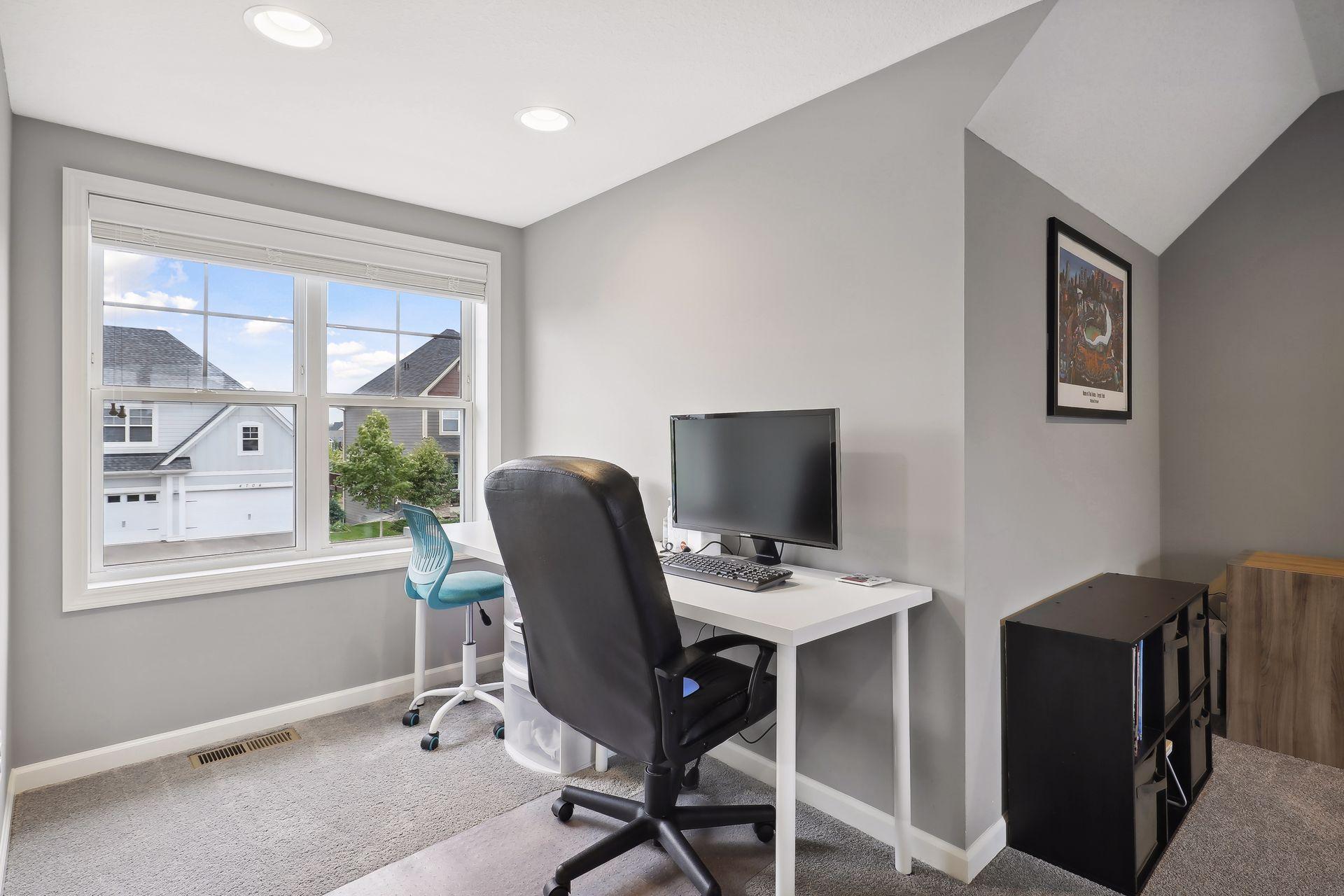 Home office with a white desk and computer beside a large window.