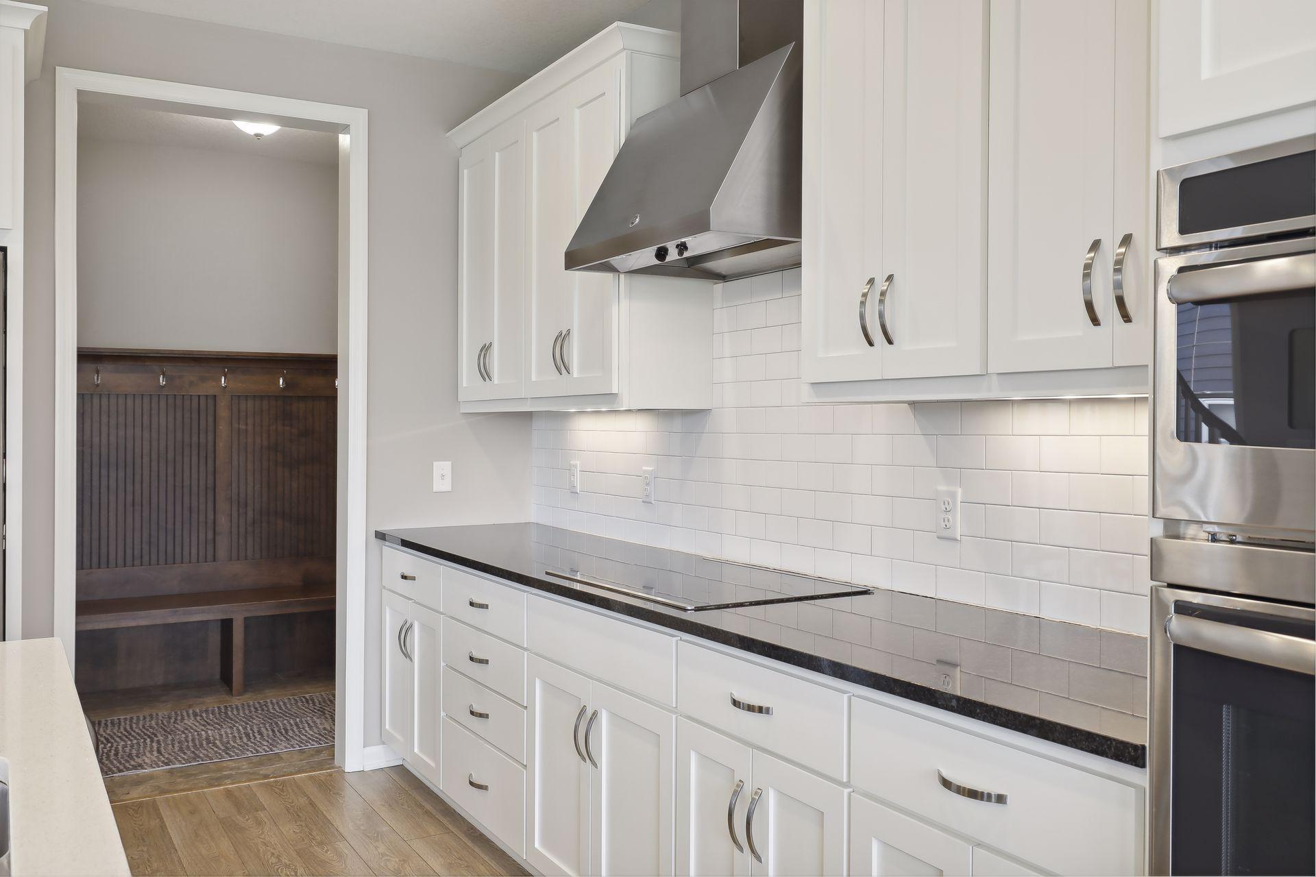 Kitchen with white cabinets, subway tile backsplash, dark counters, and a doorway to a wood-bench mudroom.