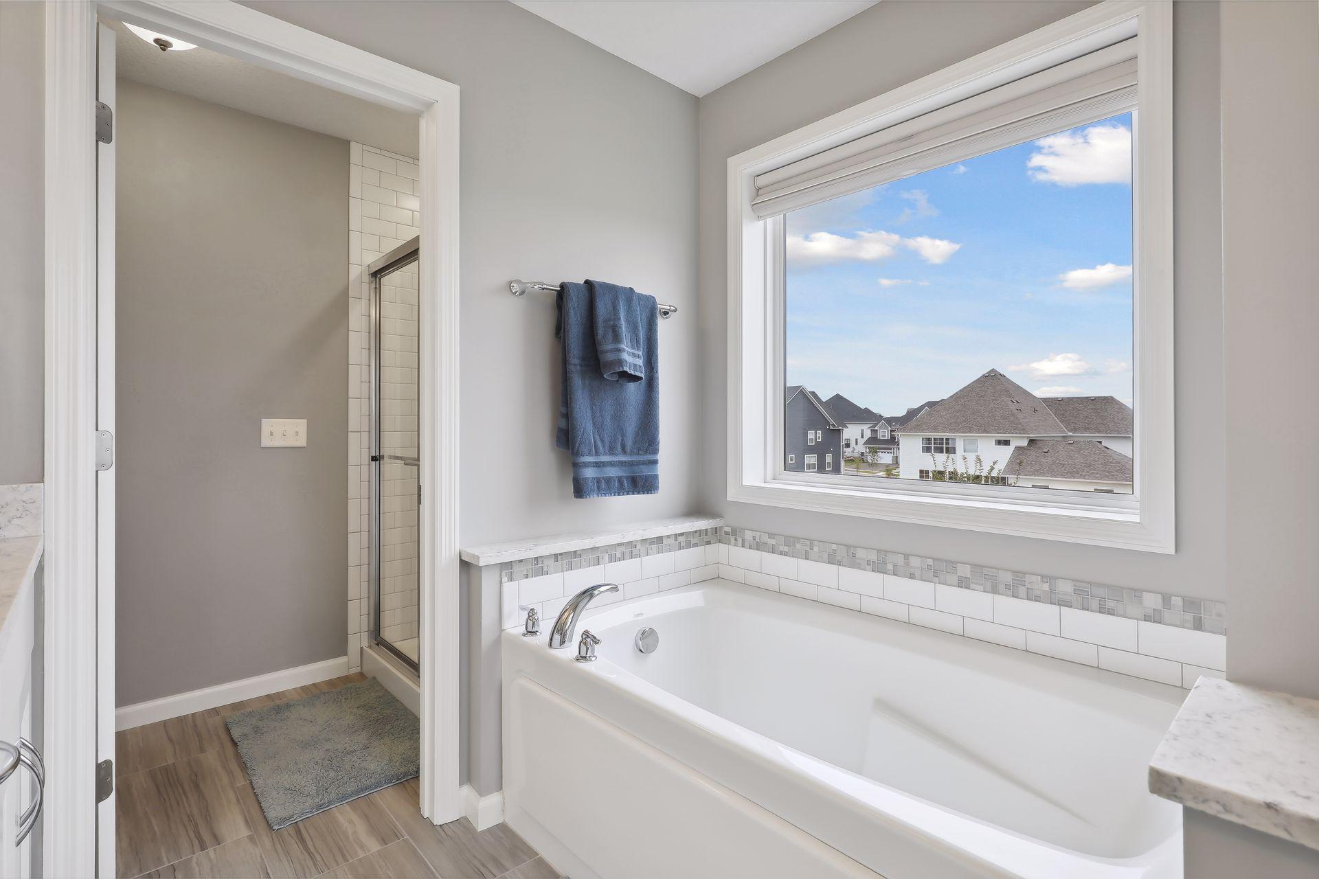 Bathroom with a white soaking tub, glass shower, and large window overlooking neighboring homes.