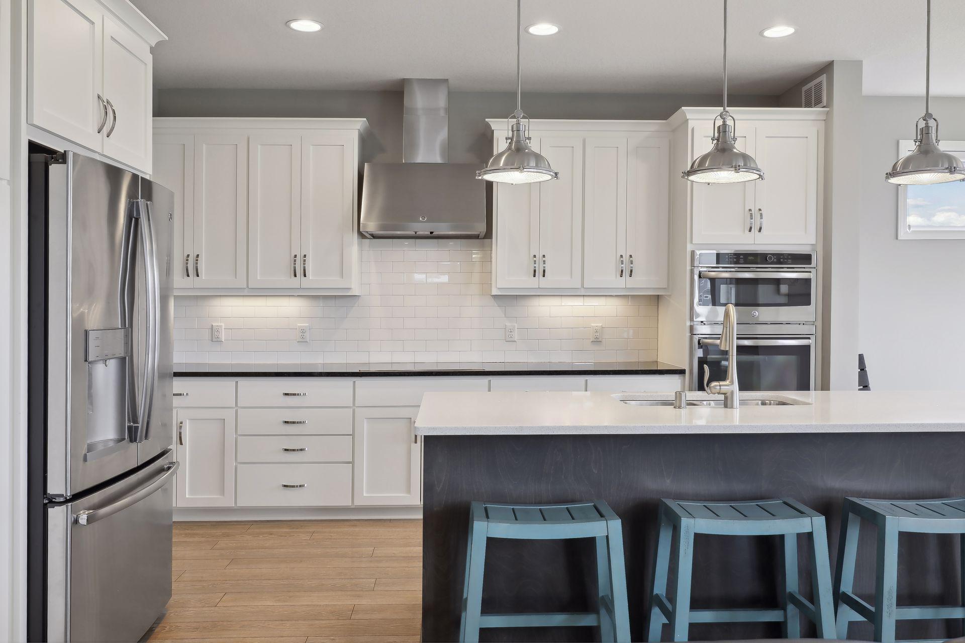 Modern kitchen with white cabinets, stainless steel appliances, and a dark island with blue stools.