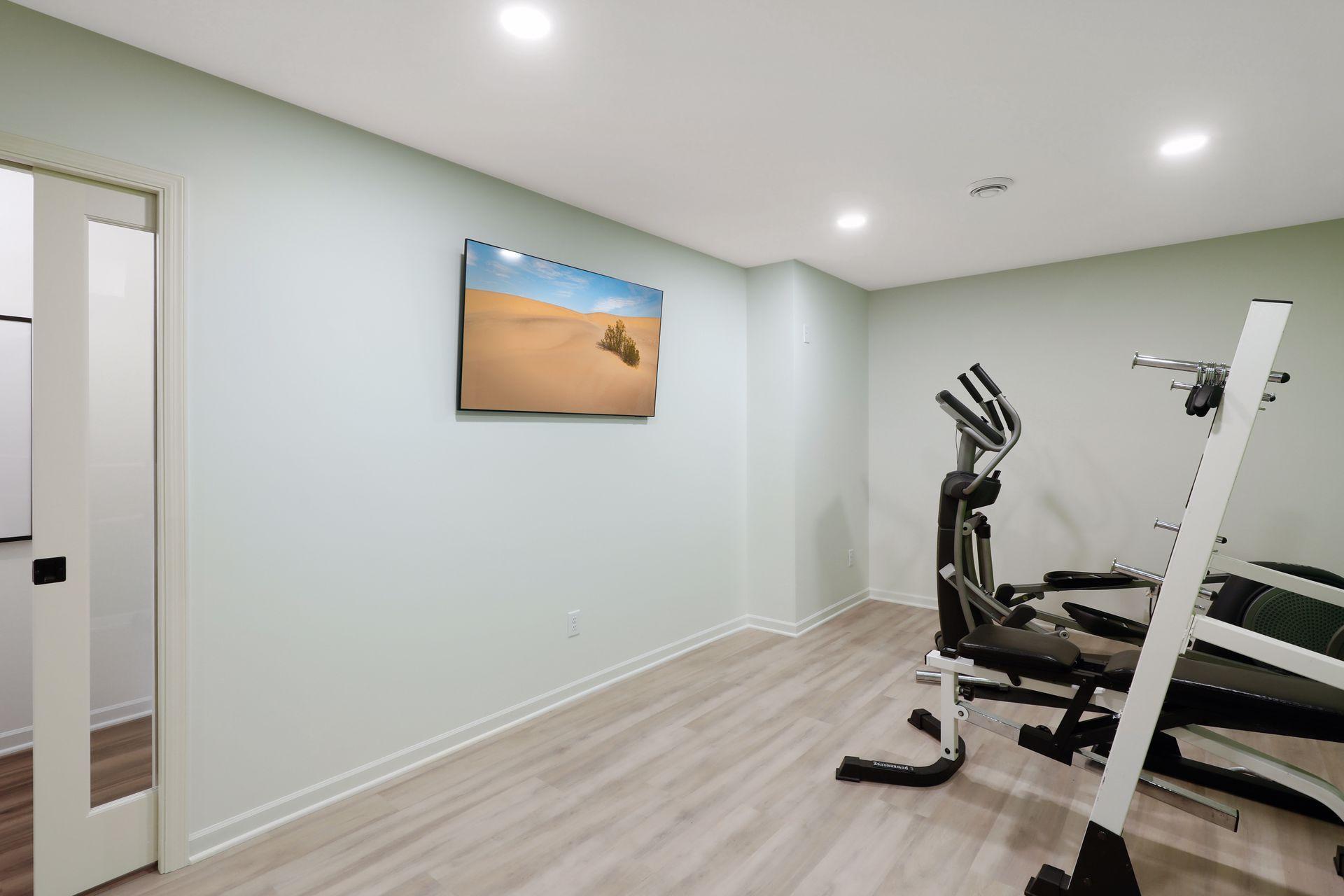 Home gym with an elliptical and weight-training equipment on light wood-look flooring.
