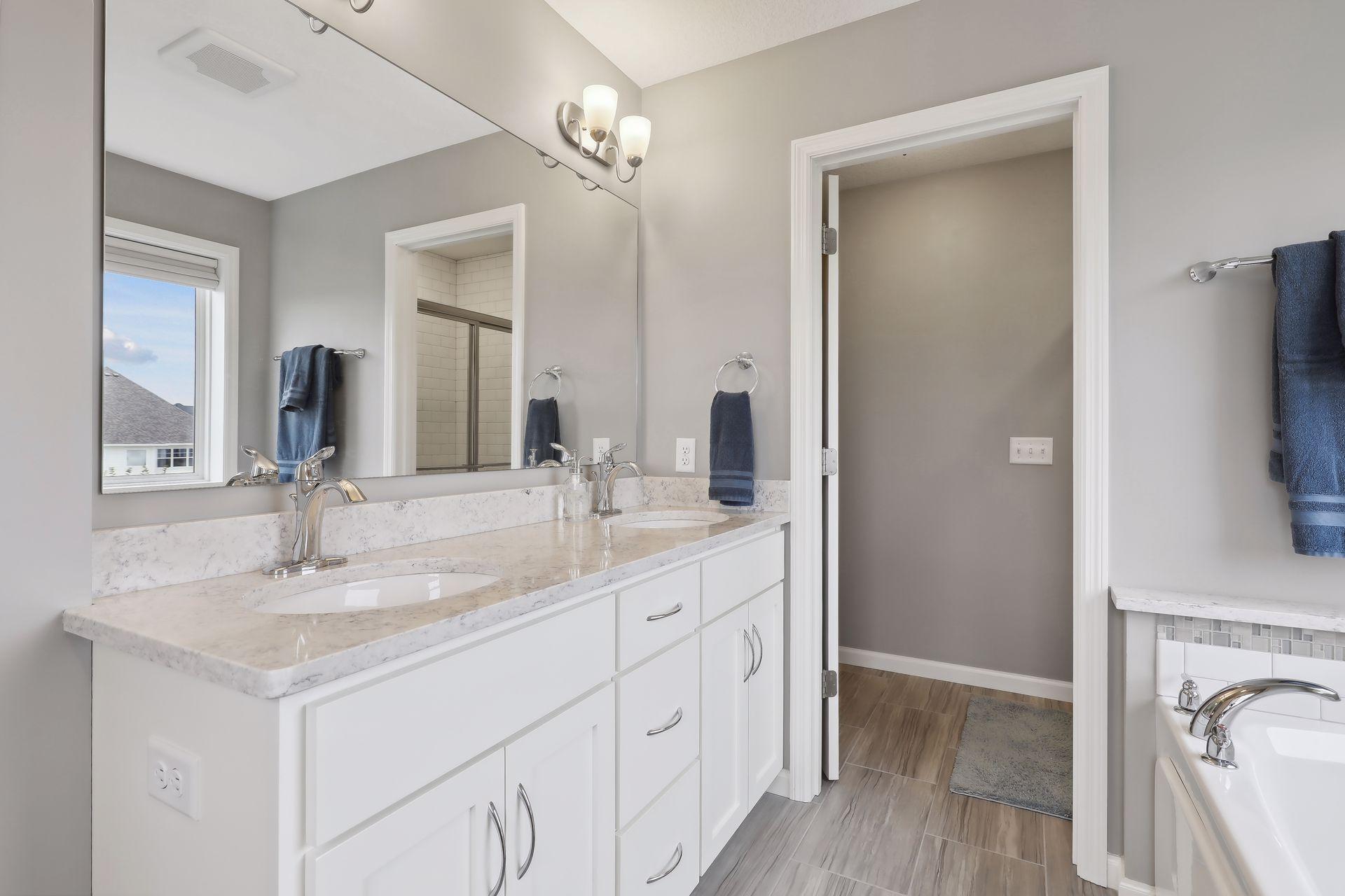 Bathroom with a long double-sink vanity, large mirror, and tiled shower visible through the doorway.