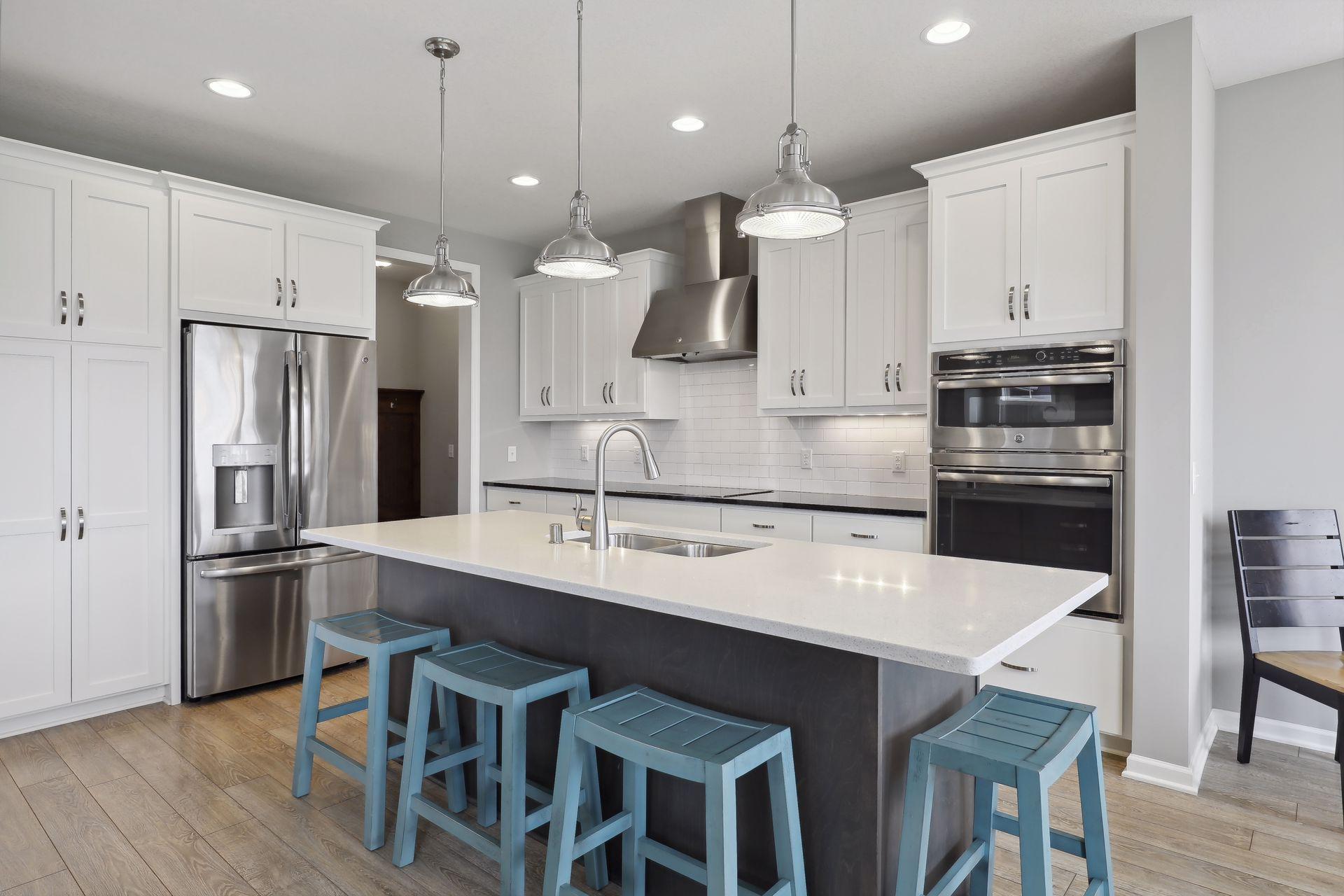 Modern kitchen with white cabinets, stainless steel appliances, and a large island lined with blue stools.