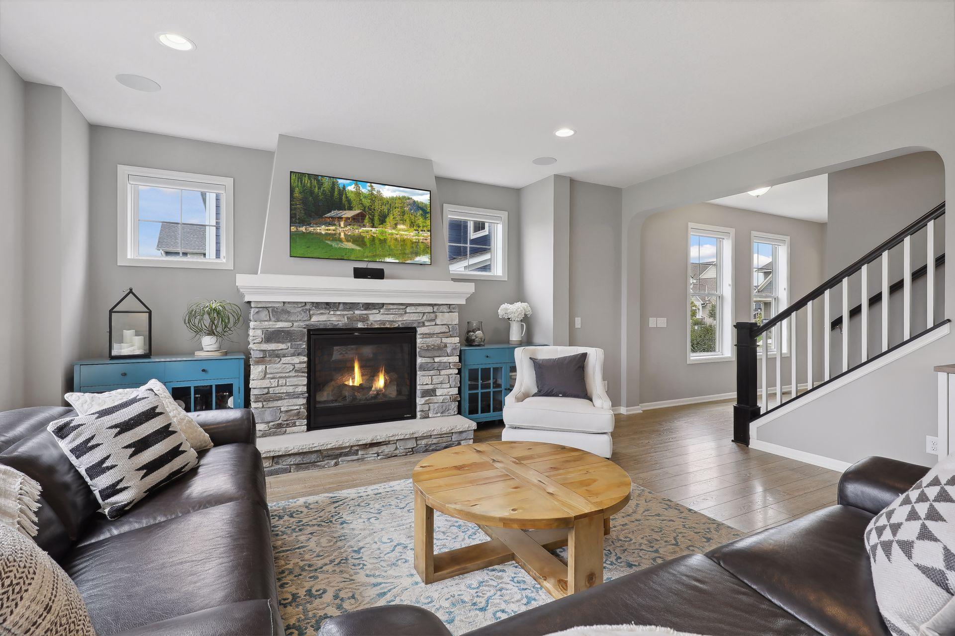 Living room with a stone fireplace, dark leather sofas, and a staircase with black railing.