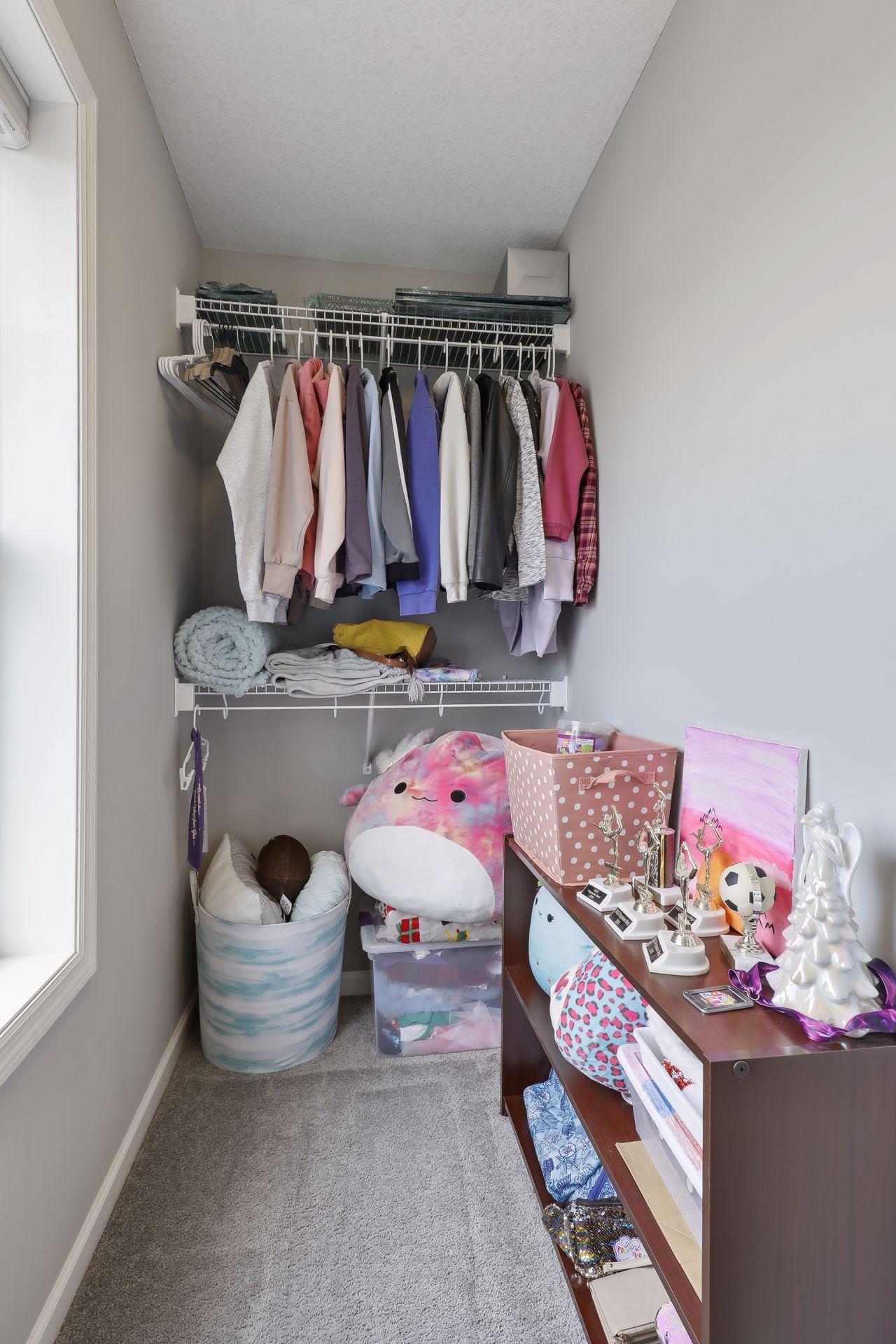 Walk-in closet with hanging clothes, stuffed toys, storage bins, and sports trophies.