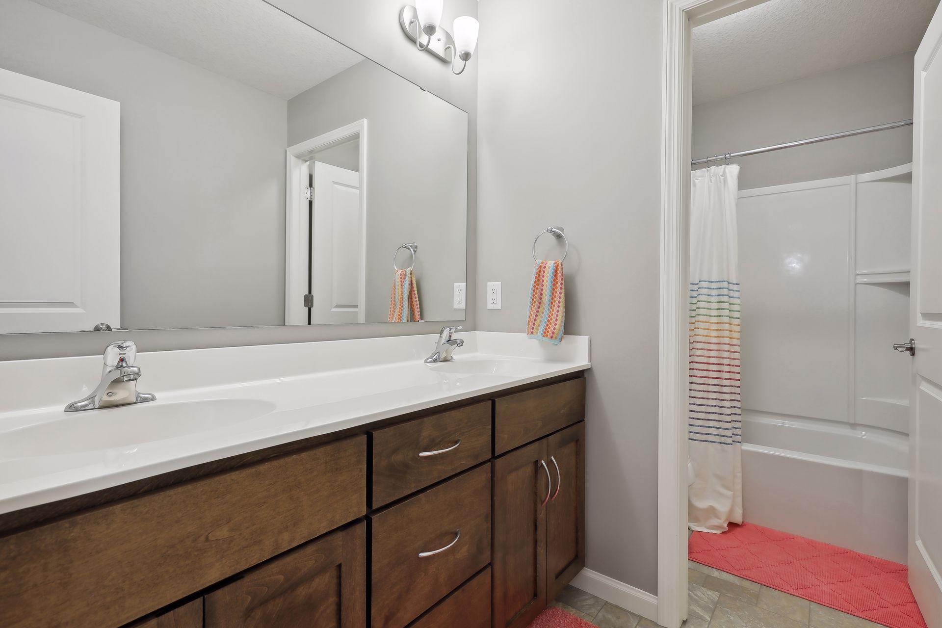 Bathroom with a double-sink dark wood vanity, large mirror, and tub-shower with striped curtain.