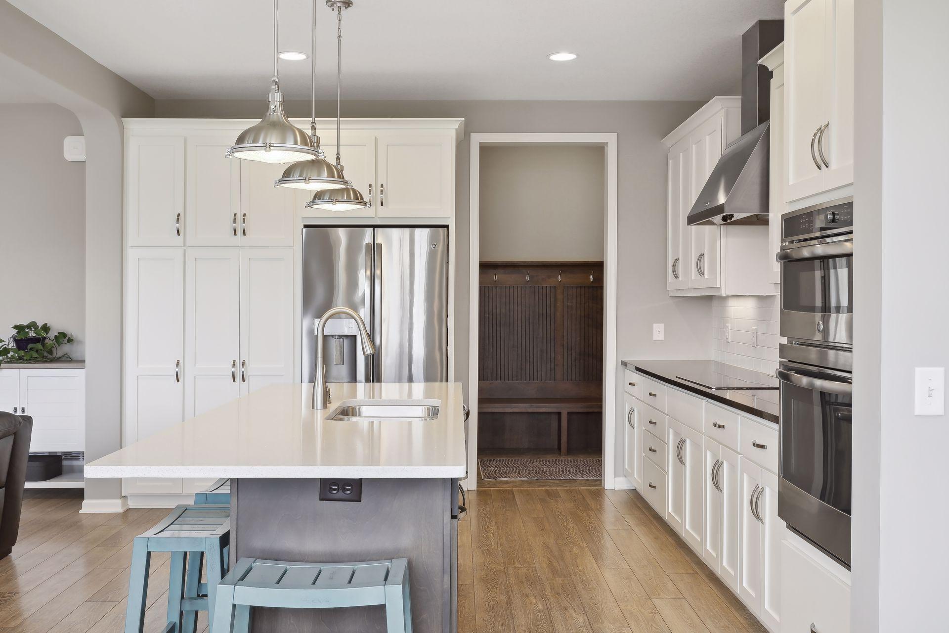 Kitchen with white cabinets, stainless steel appliances, and an island with a sink beside a built-in bench nook.